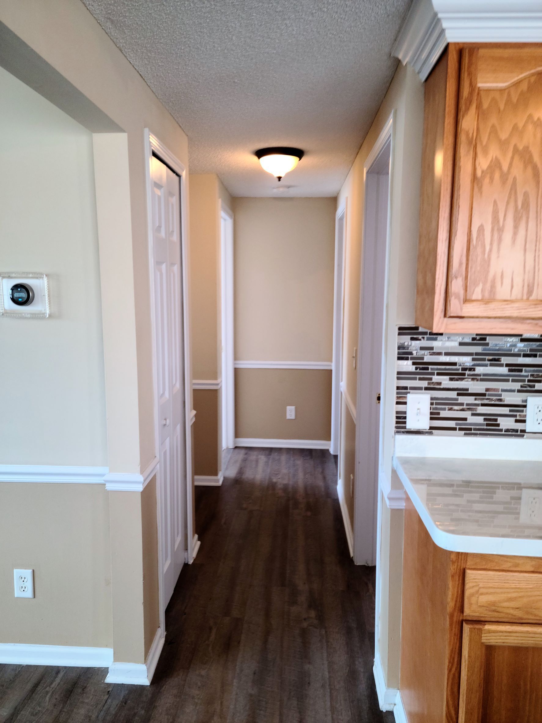 A long hallway leading to a kitchen with wooden cabinets.