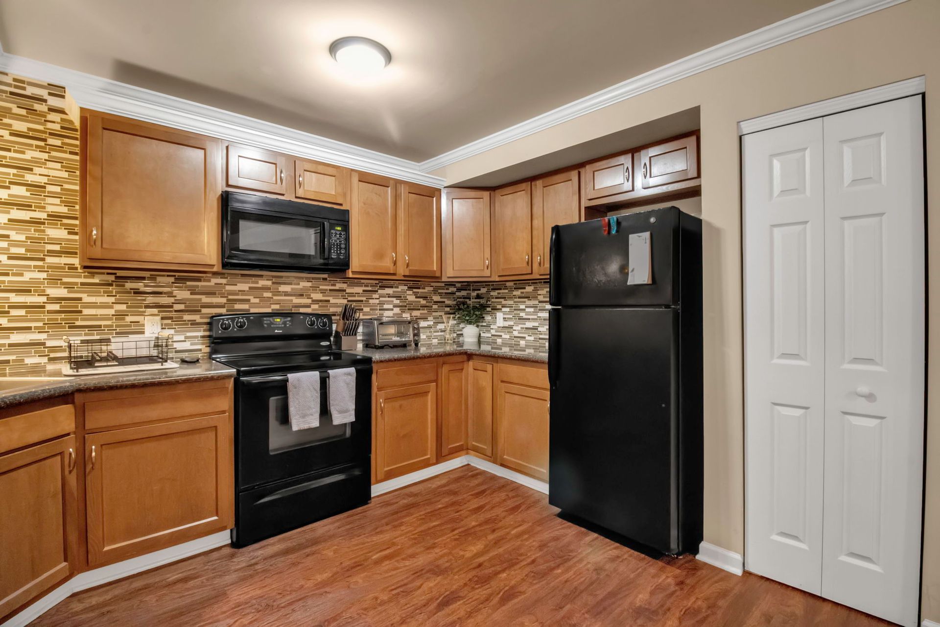 A kitchen with wooden cabinets , a black refrigerator , a stove , and a microwave.