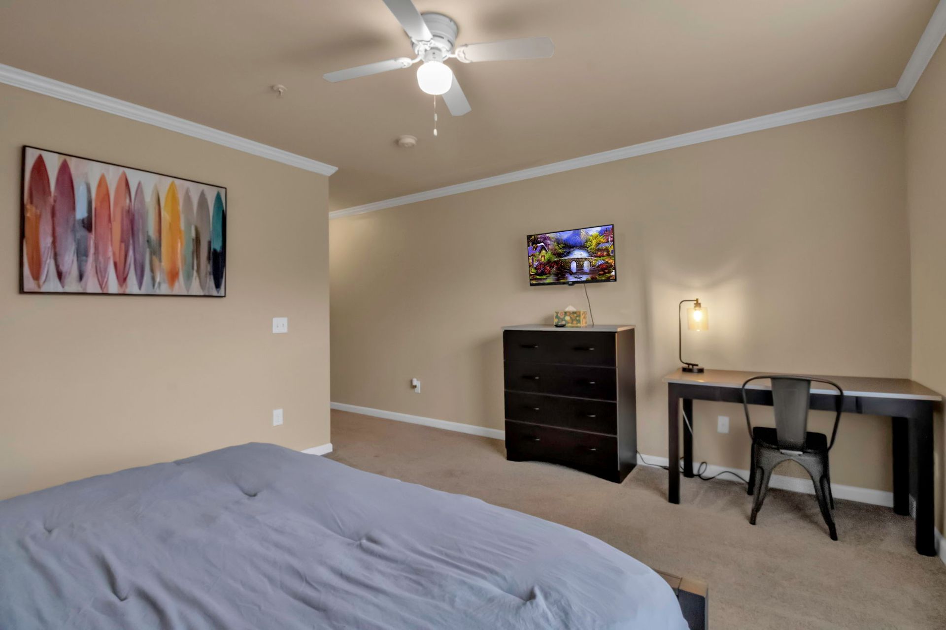 A bedroom with a bed , desk , dresser and television.