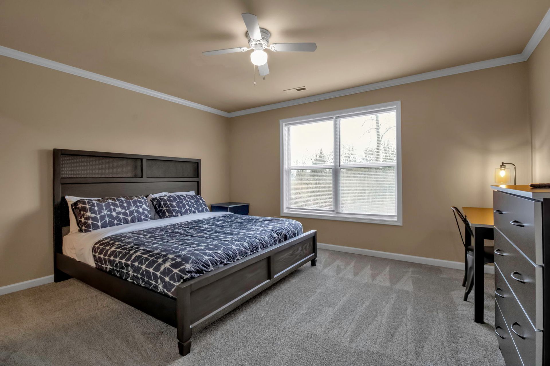 A bedroom with a king size bed , dresser , desk and ceiling fan.