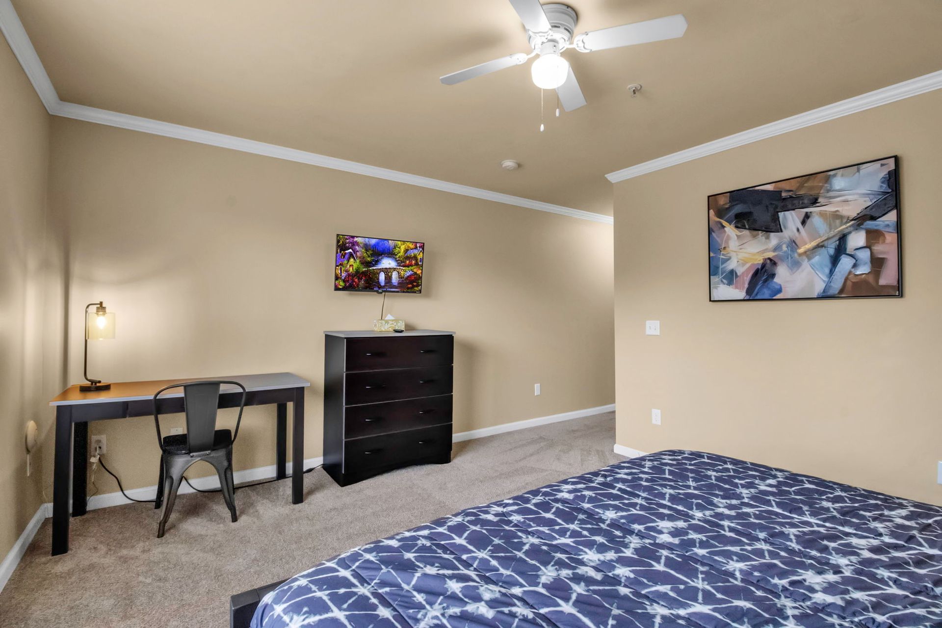 A bedroom with a bed , desk , chairs and a ceiling fan.
