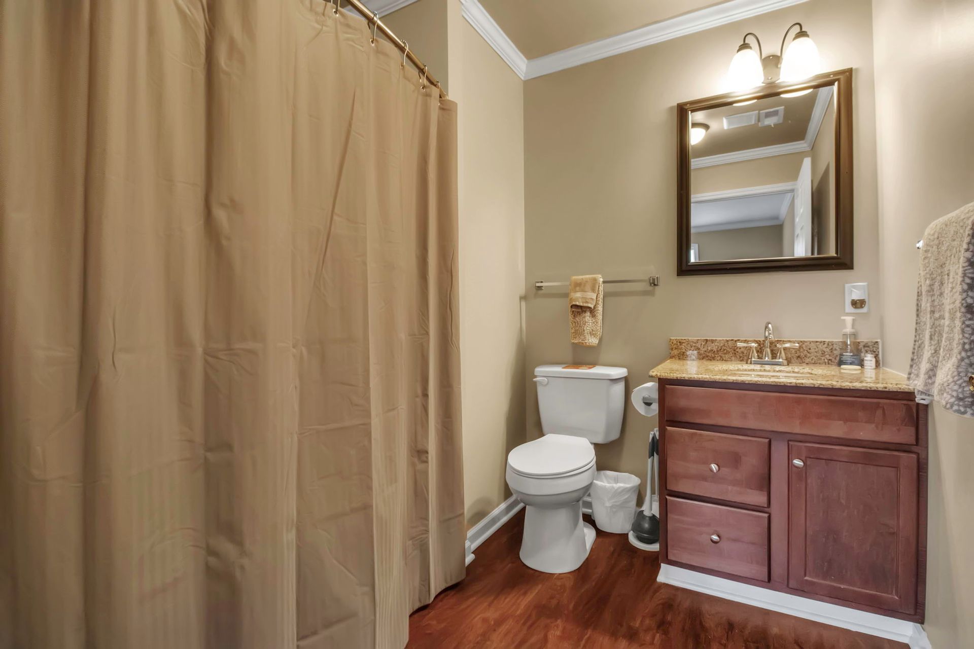 A bathroom with a toilet , sink , mirror and shower curtain.