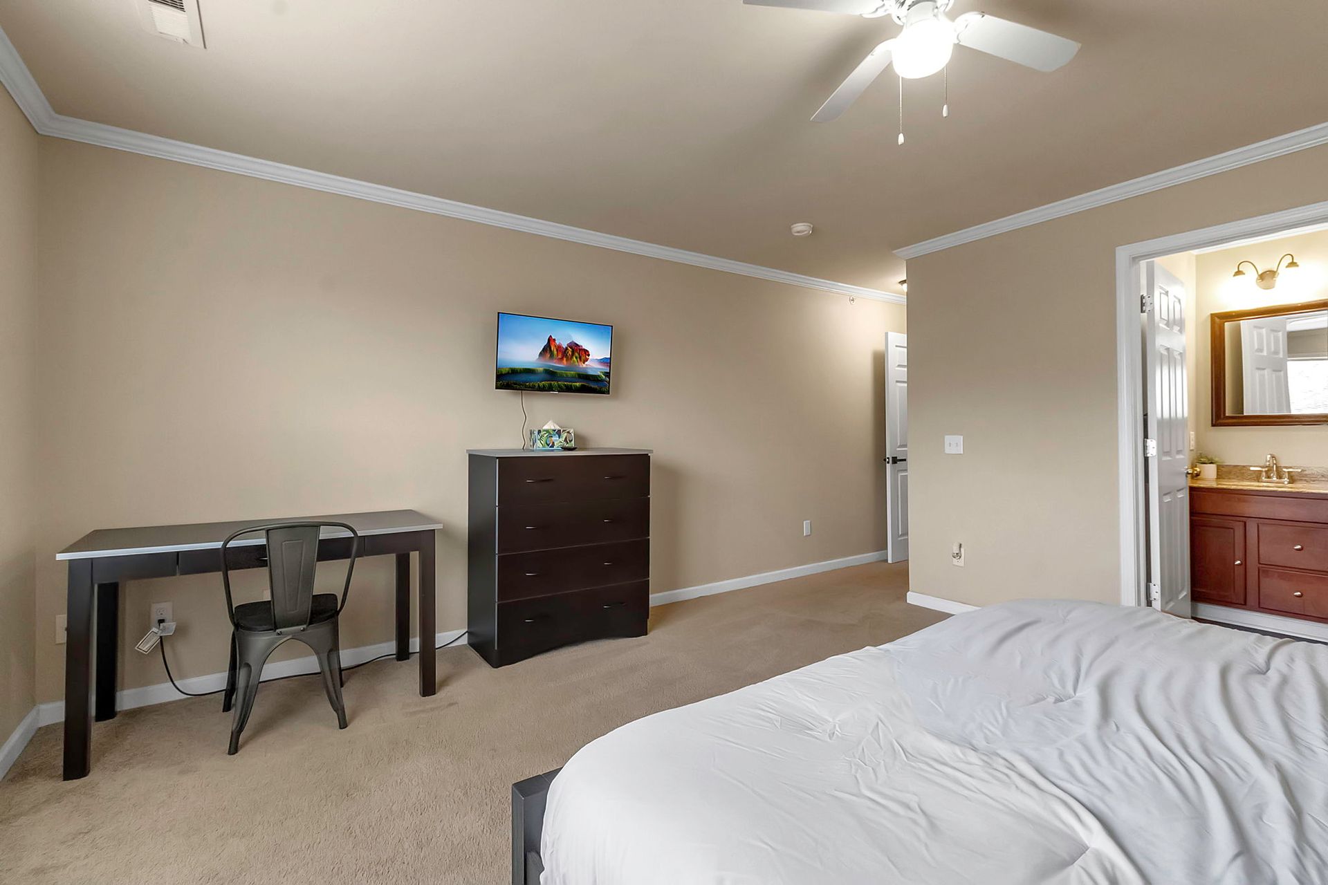 A bedroom with a bed , desk , dresser and television.