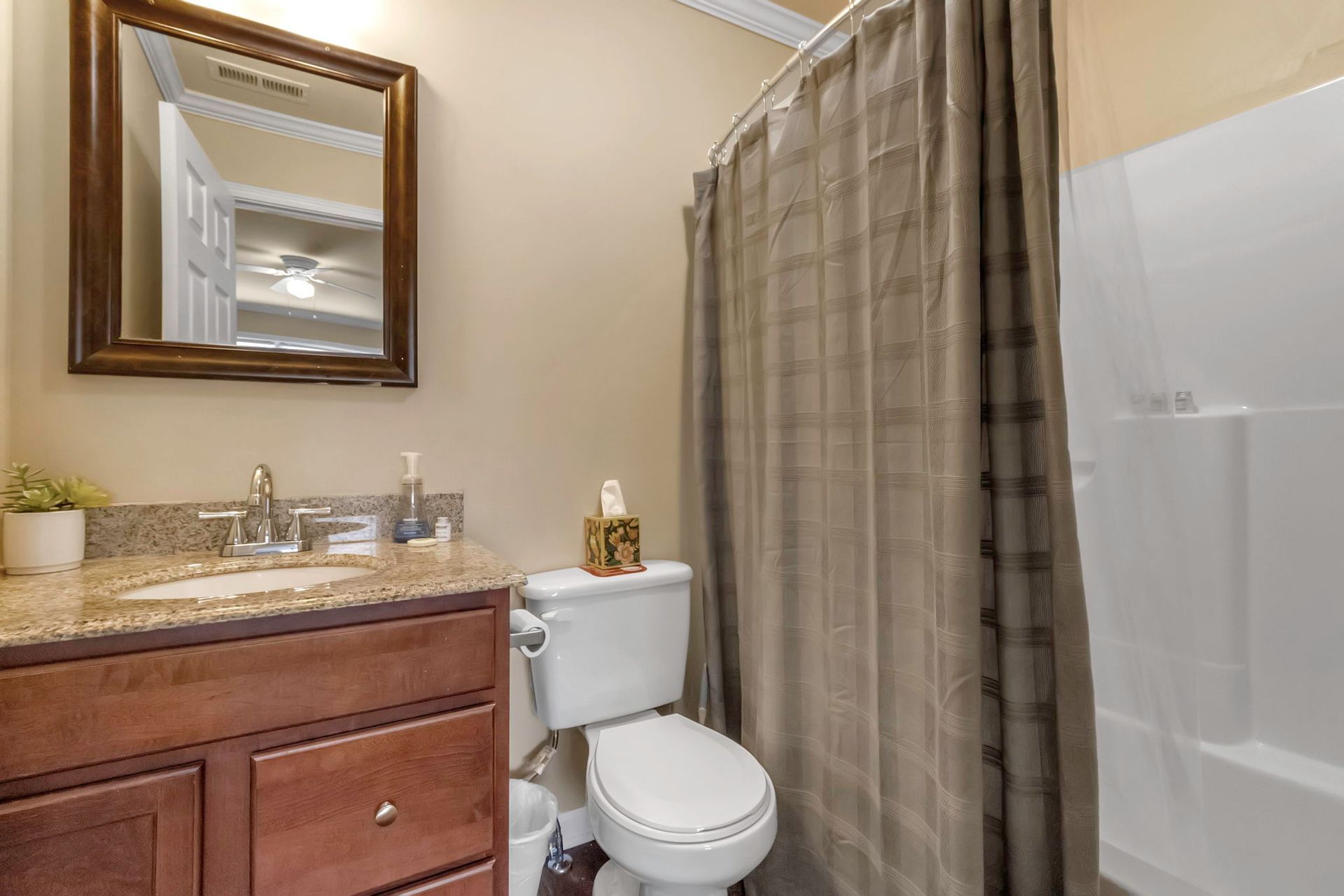 A bathroom with a toilet , sink , mirror and shower curtain.