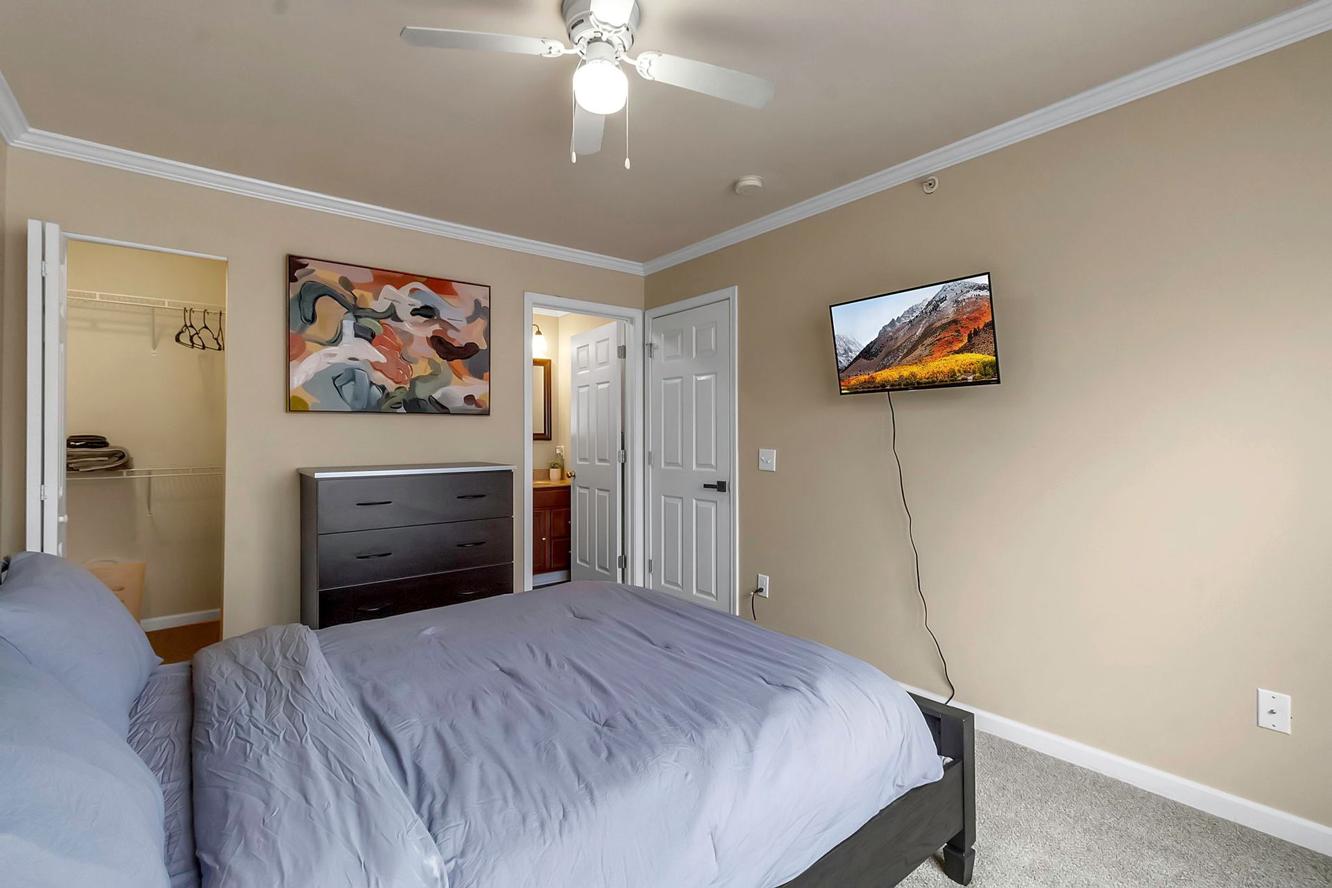 A bedroom with a bed , dresser , television and ceiling fan.