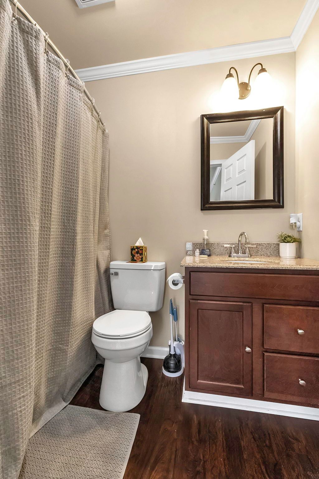A bathroom with a toilet , sink , mirror and shower curtain.