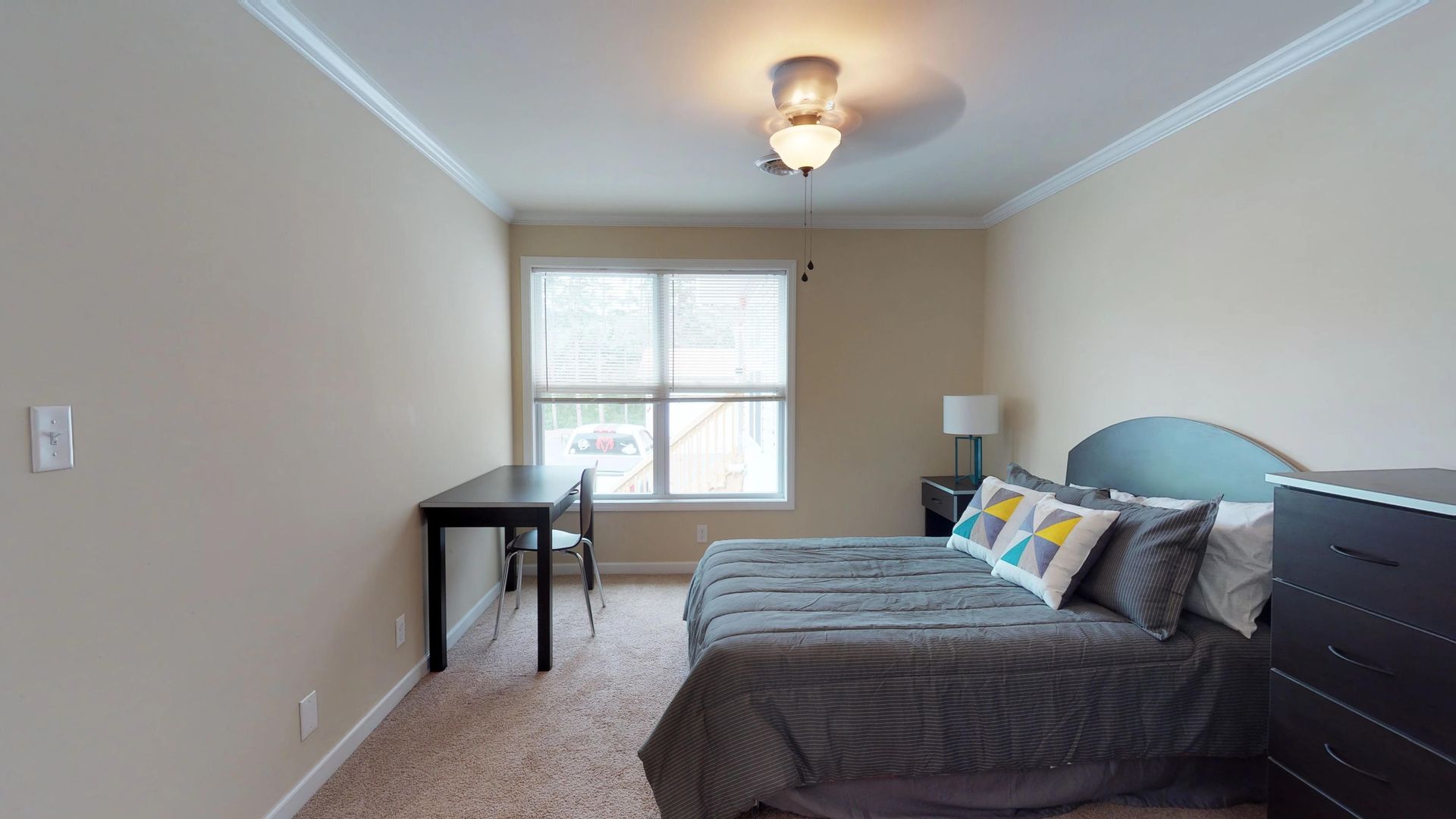 A bedroom with a bed , dresser , desk and ceiling fan.
