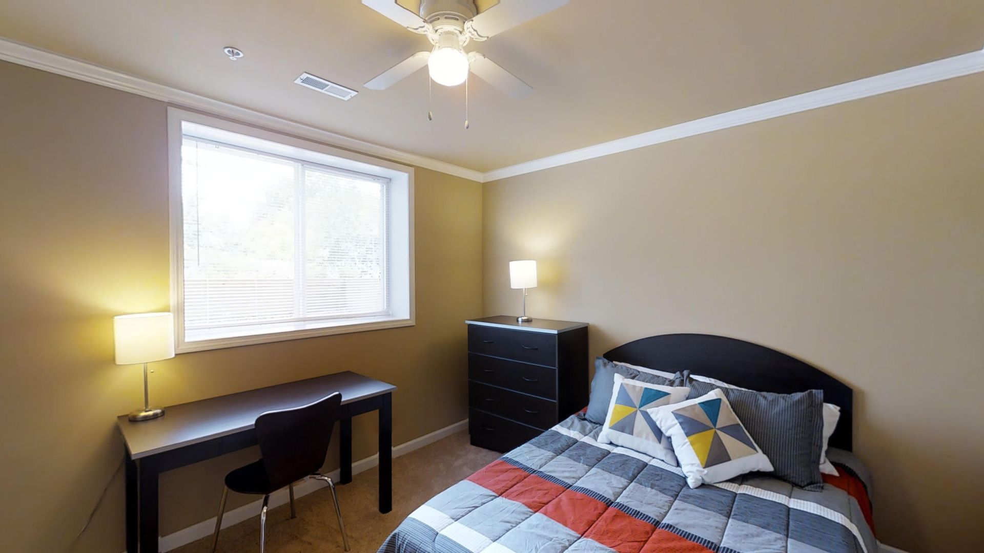 A bedroom with a bed , desk , dresser and ceiling fan.