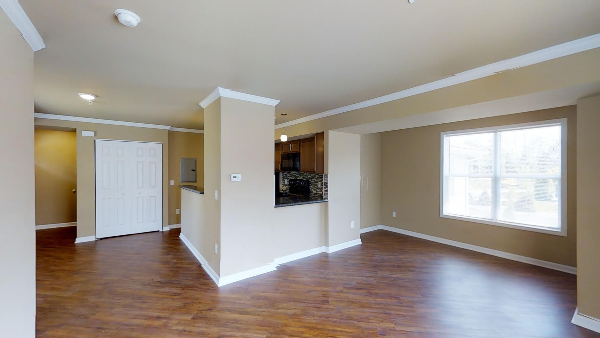 An empty living room with hardwood floors and a kitchen in the background.