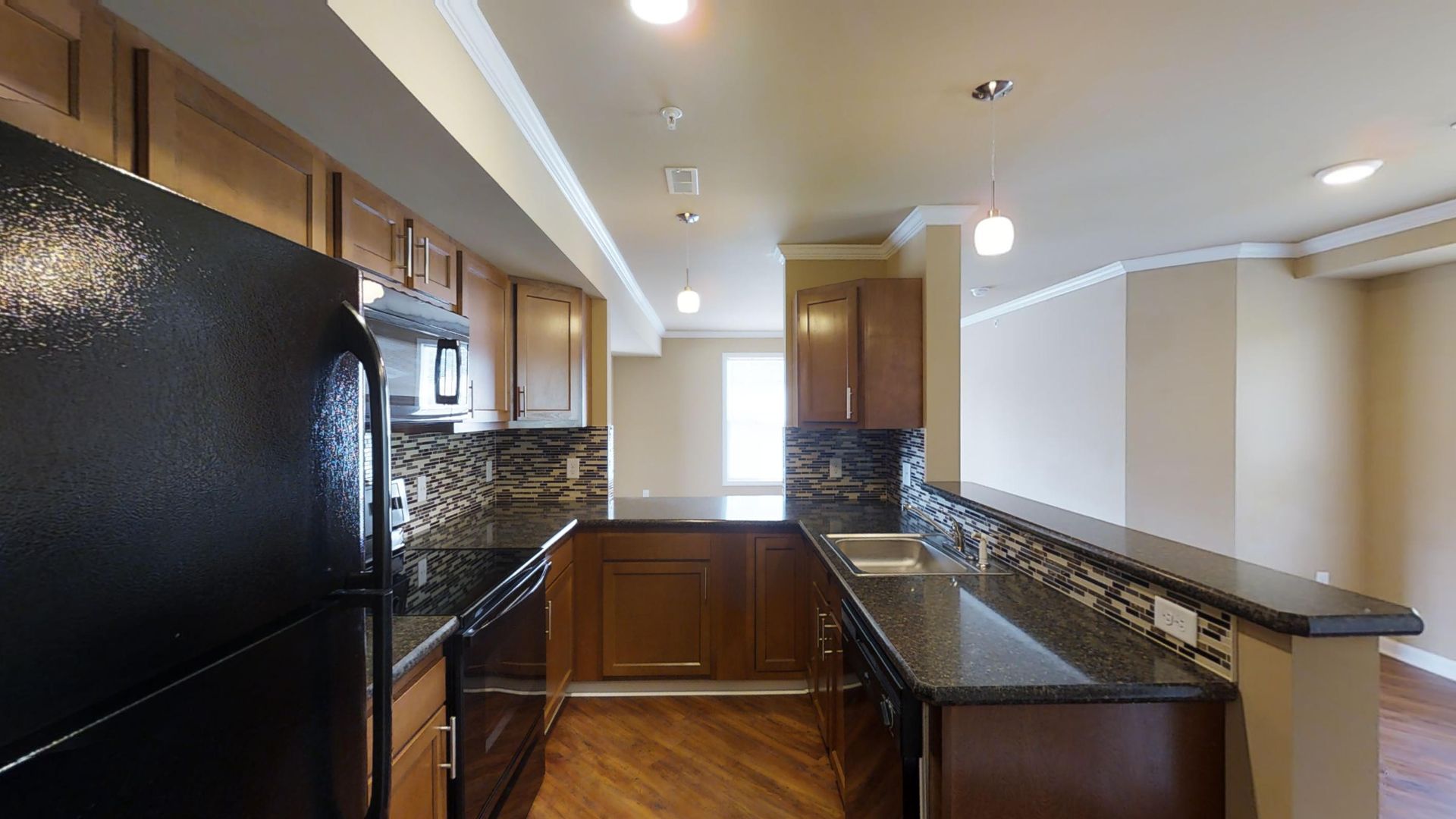 A kitchen with a black refrigerator , black appliances , granite counter tops and wooden cabinets.