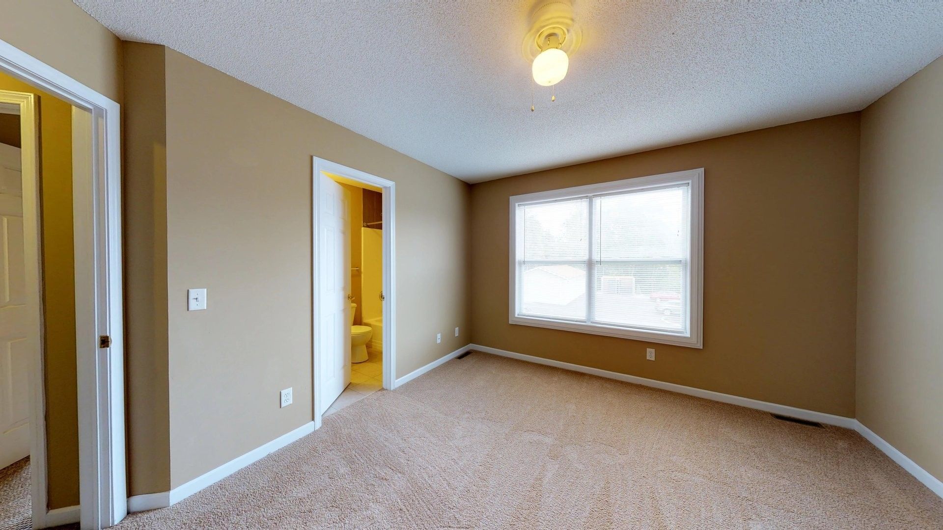An empty bedroom with a large window and a carpeted floor.