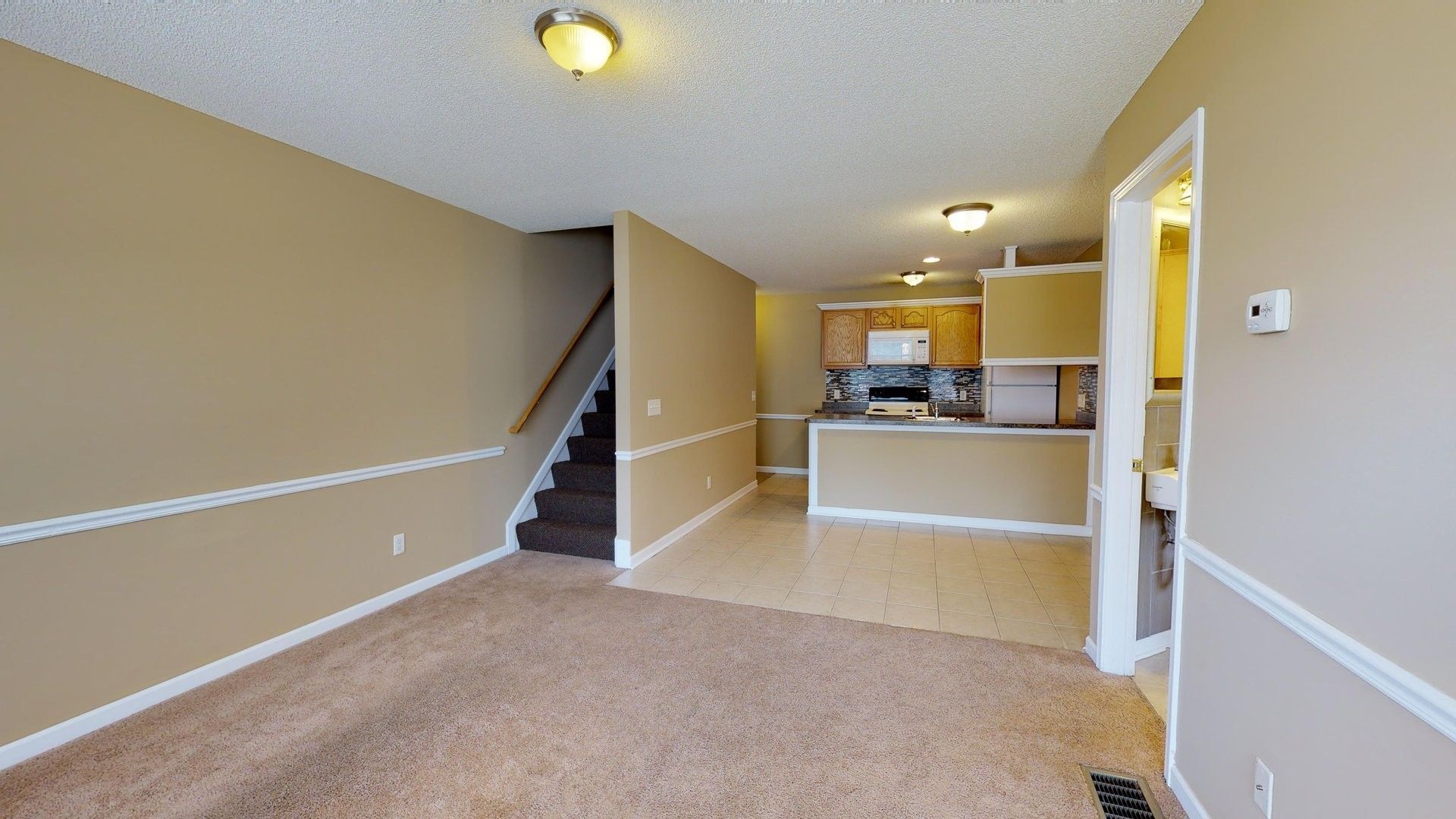 An empty living room with a staircase leading to the kitchen.