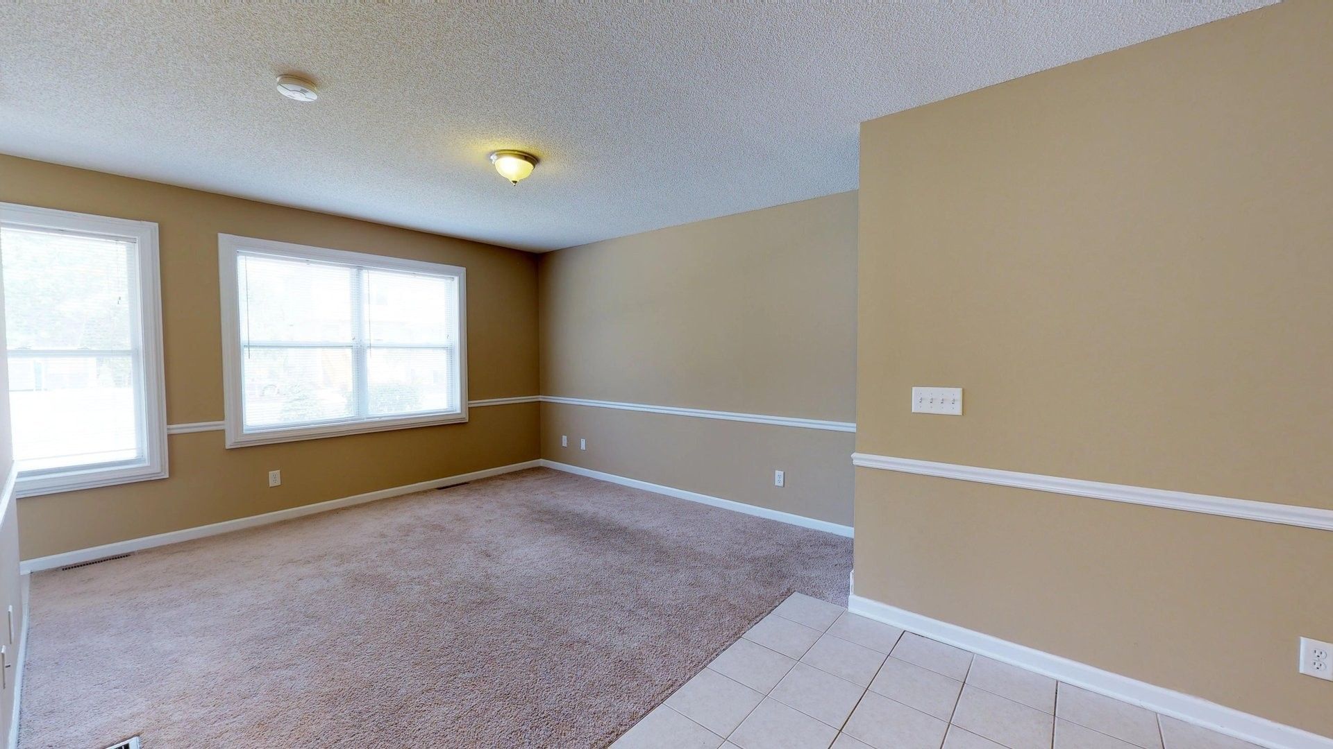 An empty living room with a carpeted floor and two windows.