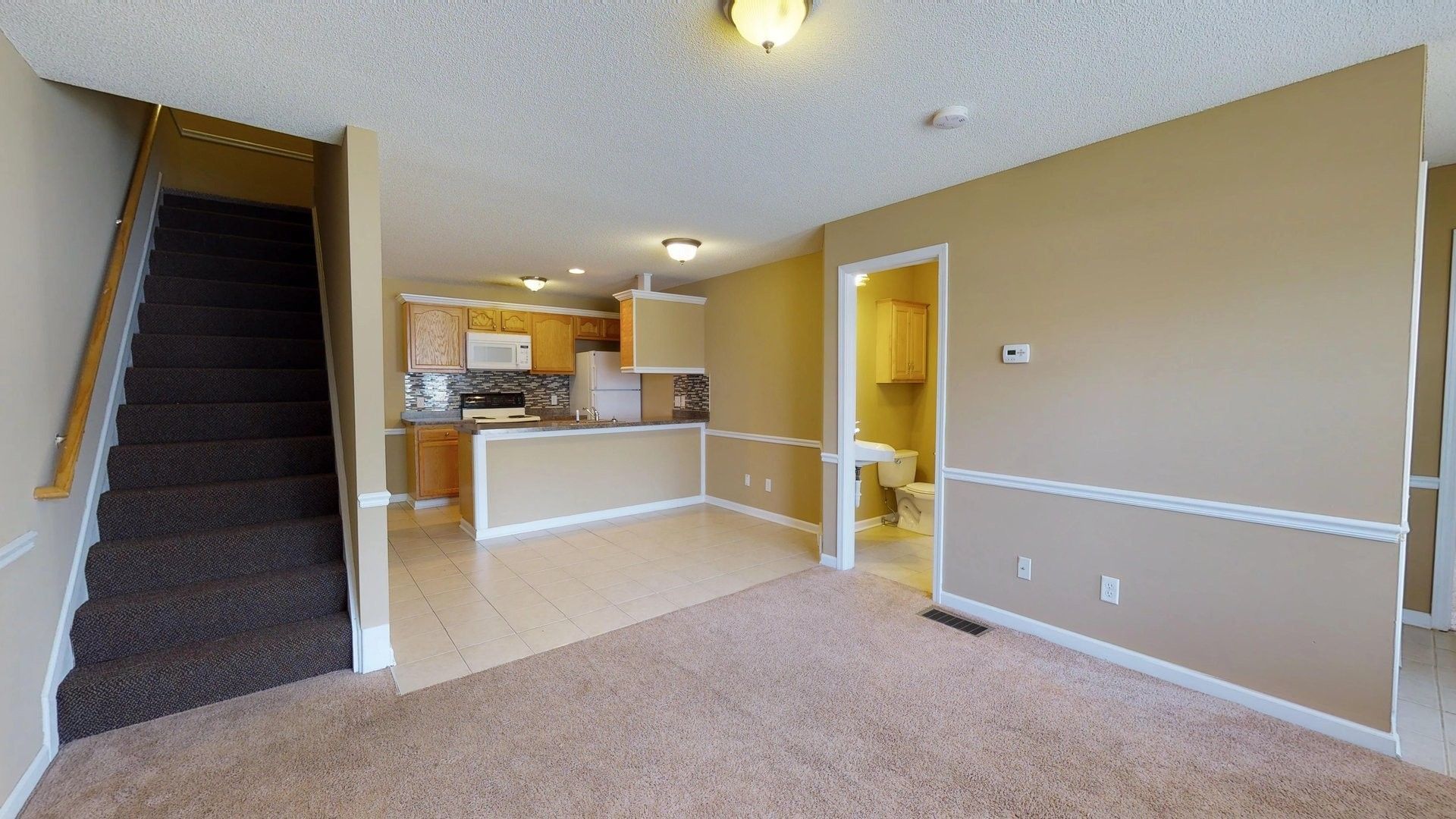 A living room with stairs leading up to the second floor and a kitchen.