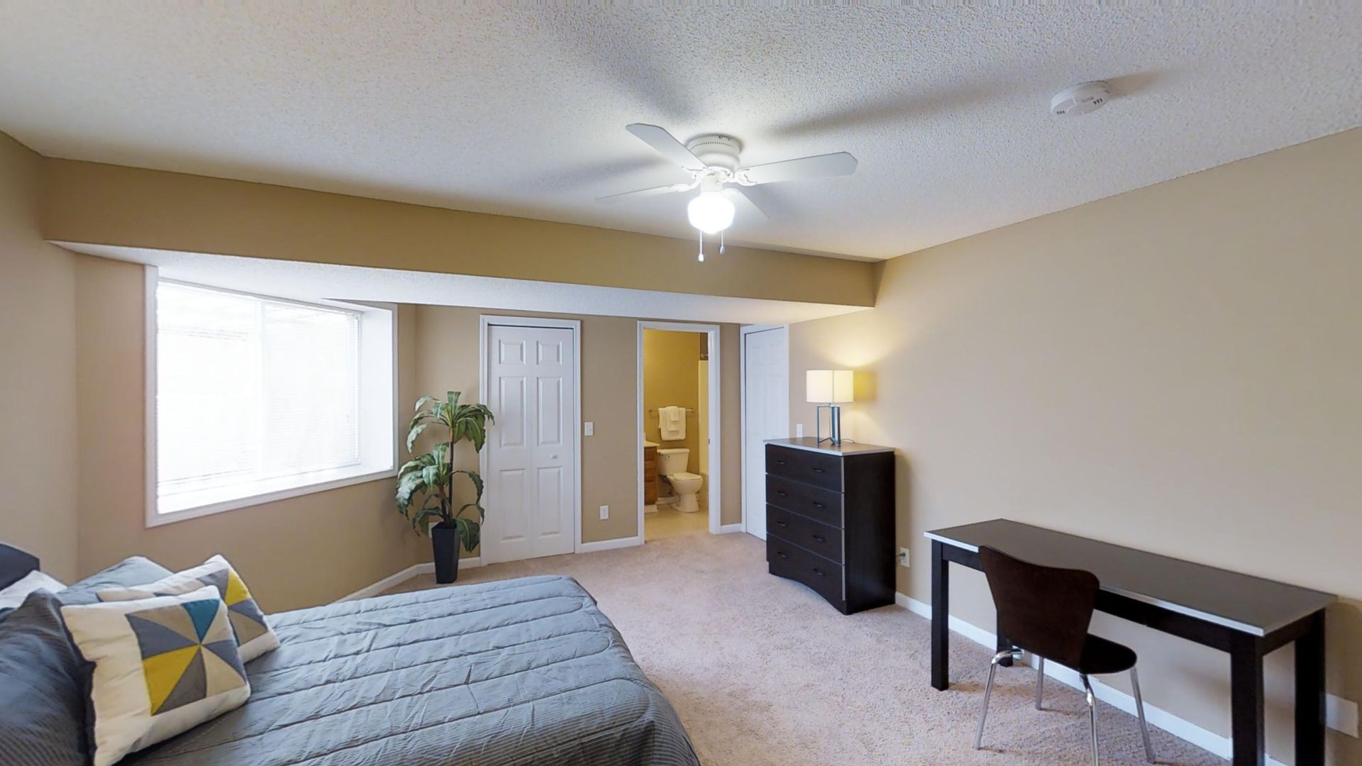 A bedroom with a bed , desk , chair and ceiling fan.