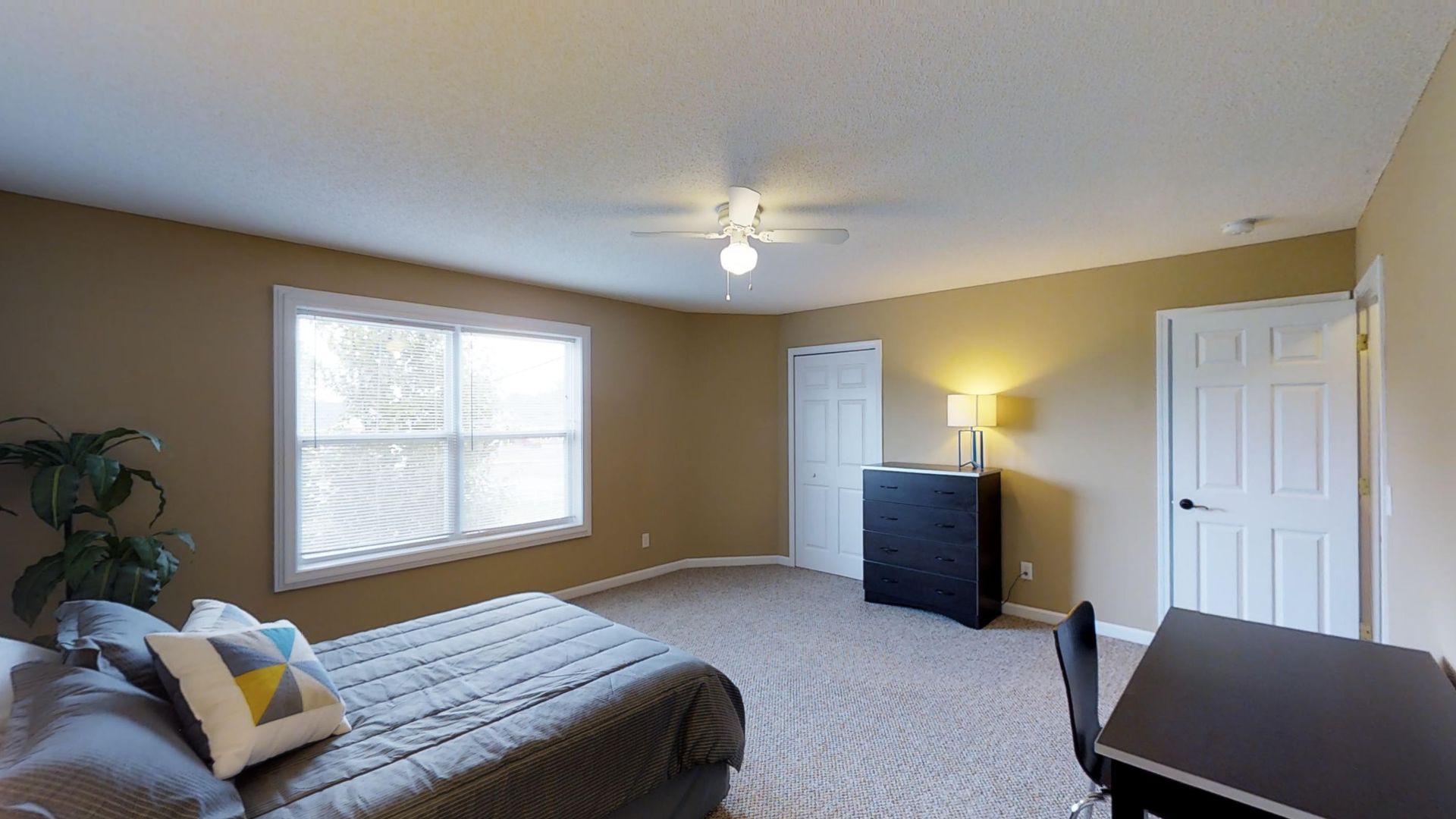 A bedroom with a bed , dresser , desk and window.