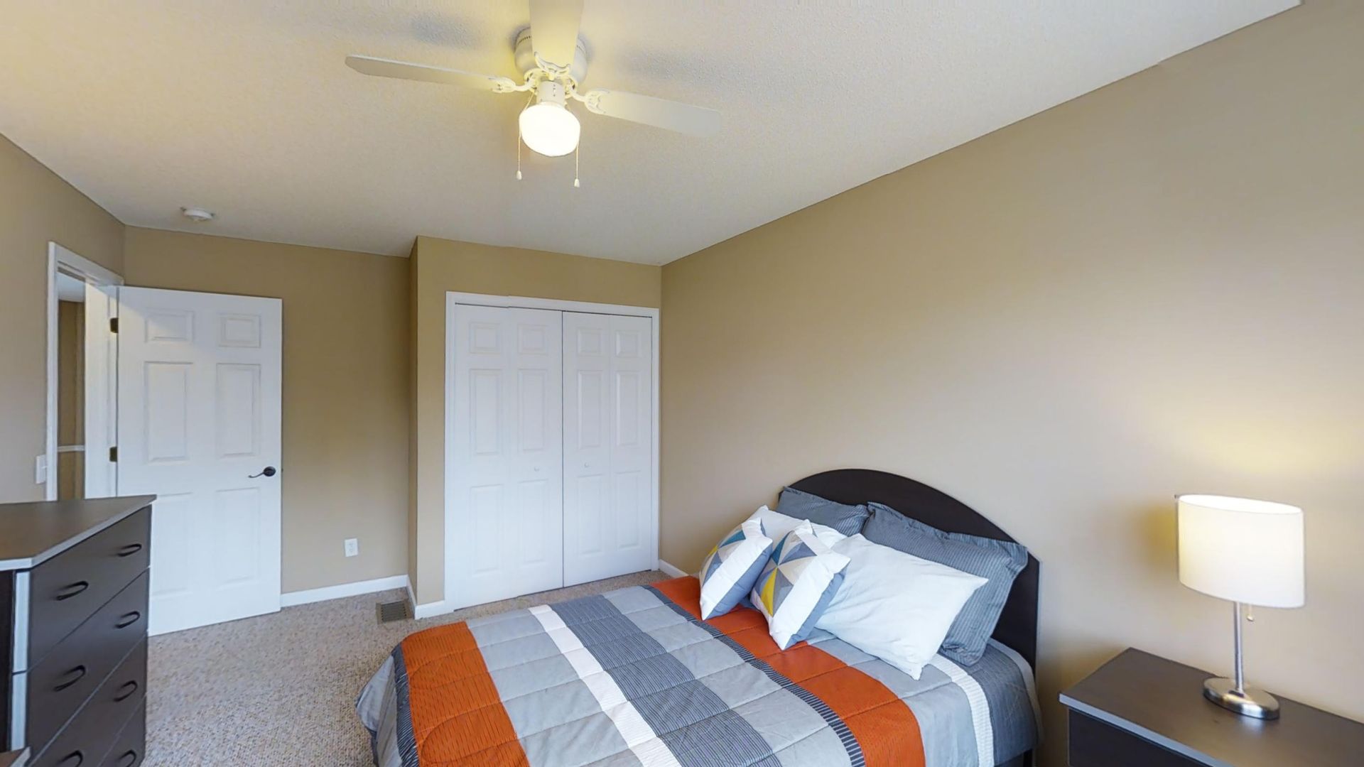 A bedroom with a bed , nightstand , dresser and ceiling fan.
