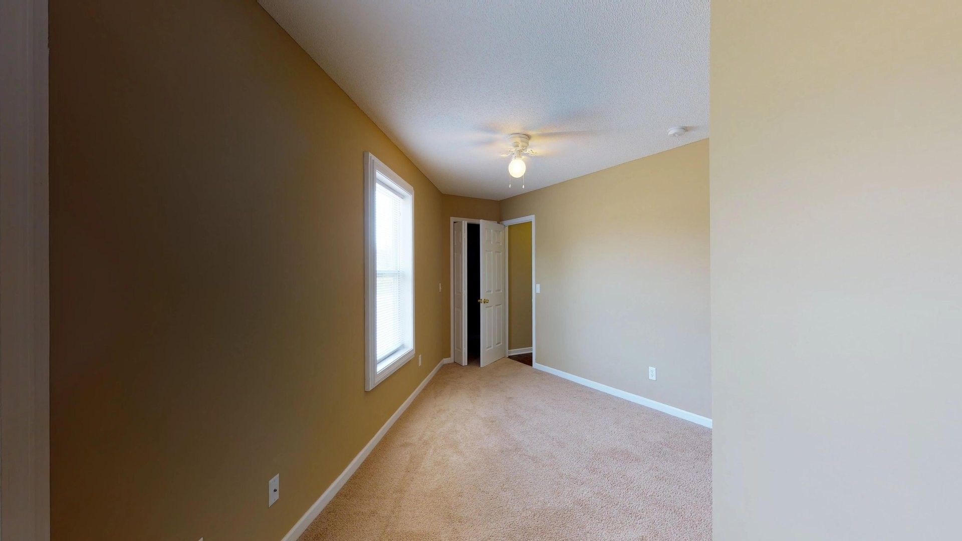 An empty bedroom with a ceiling fan and a window.