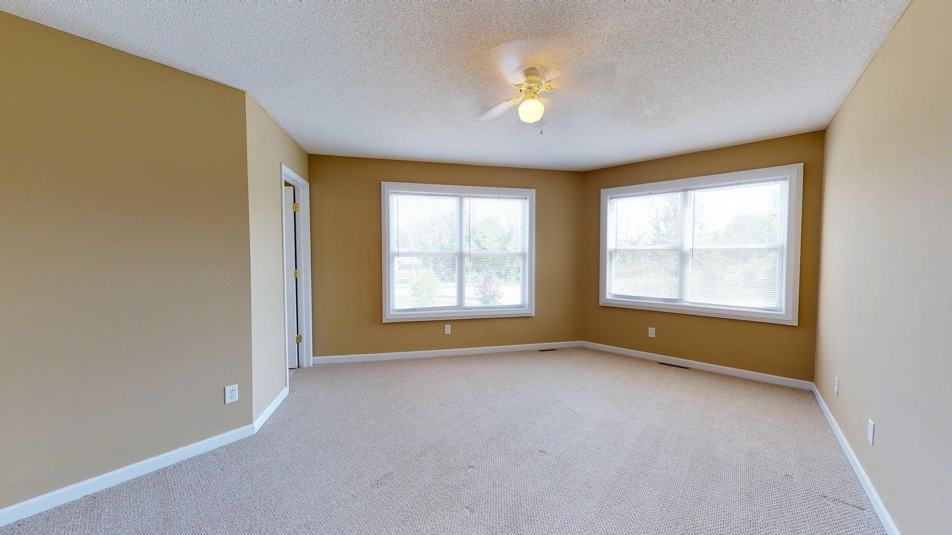 An empty living room with a ceiling fan and two windows.