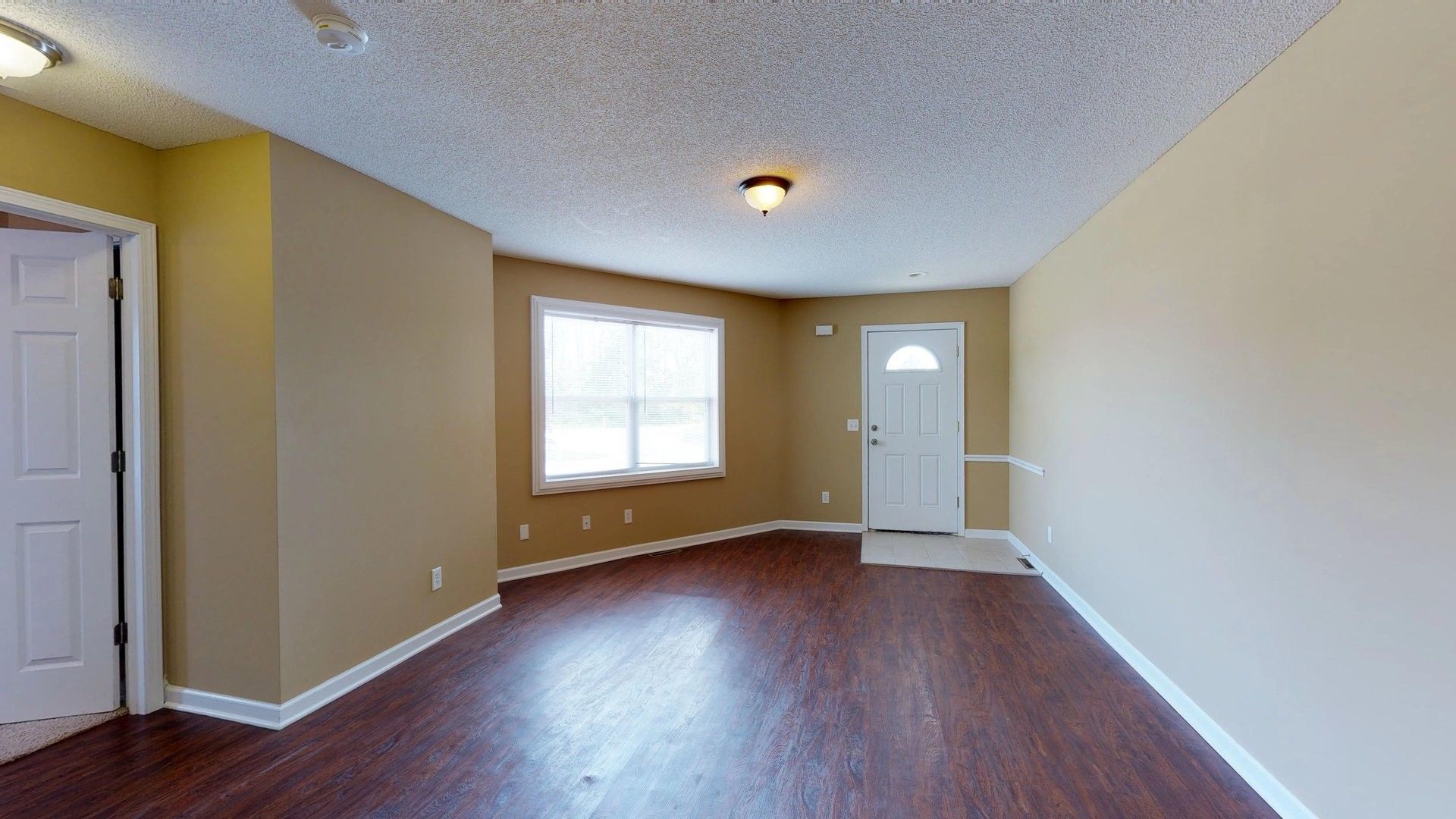 An empty living room with hardwood floors and a window.