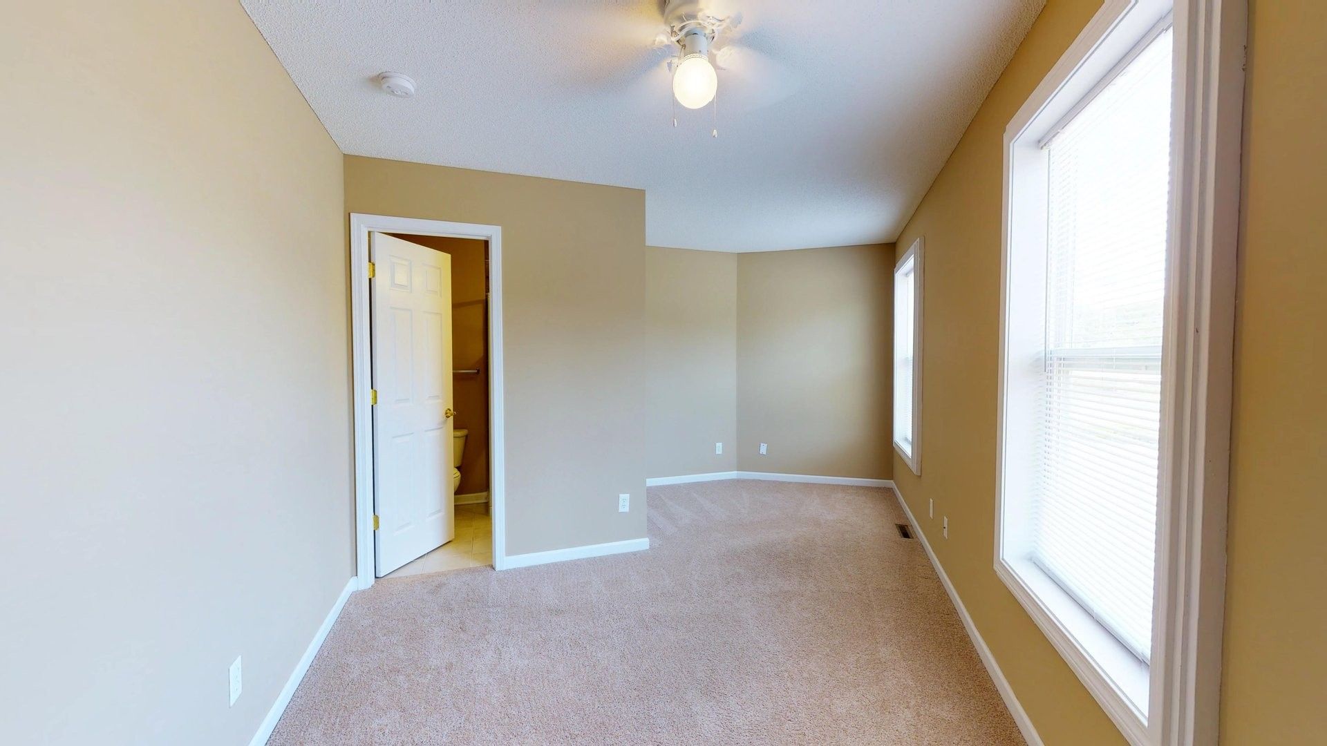 An empty bedroom with a ceiling fan and two windows.