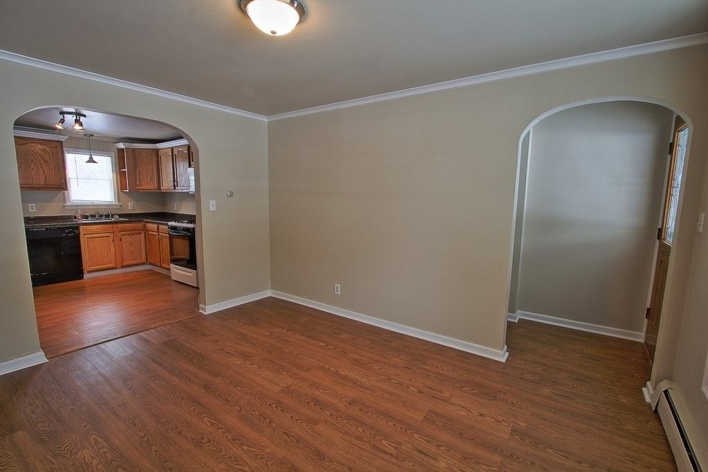 An empty living room with hardwood floors and a kitchen in the background.