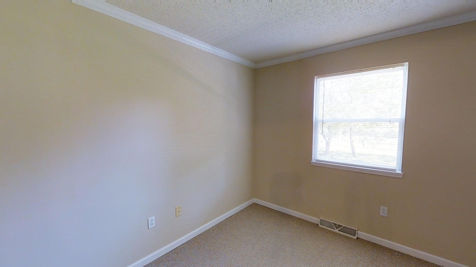 An empty bedroom with a window and carpet.