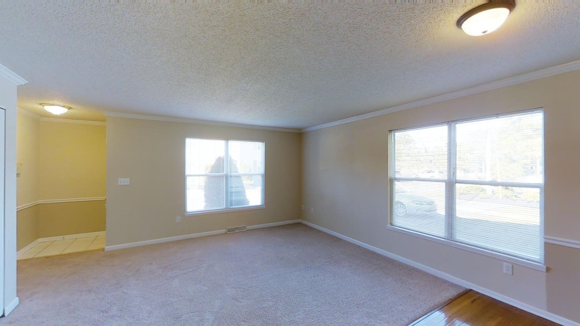 An empty living room with a lot of windows and carpet.
