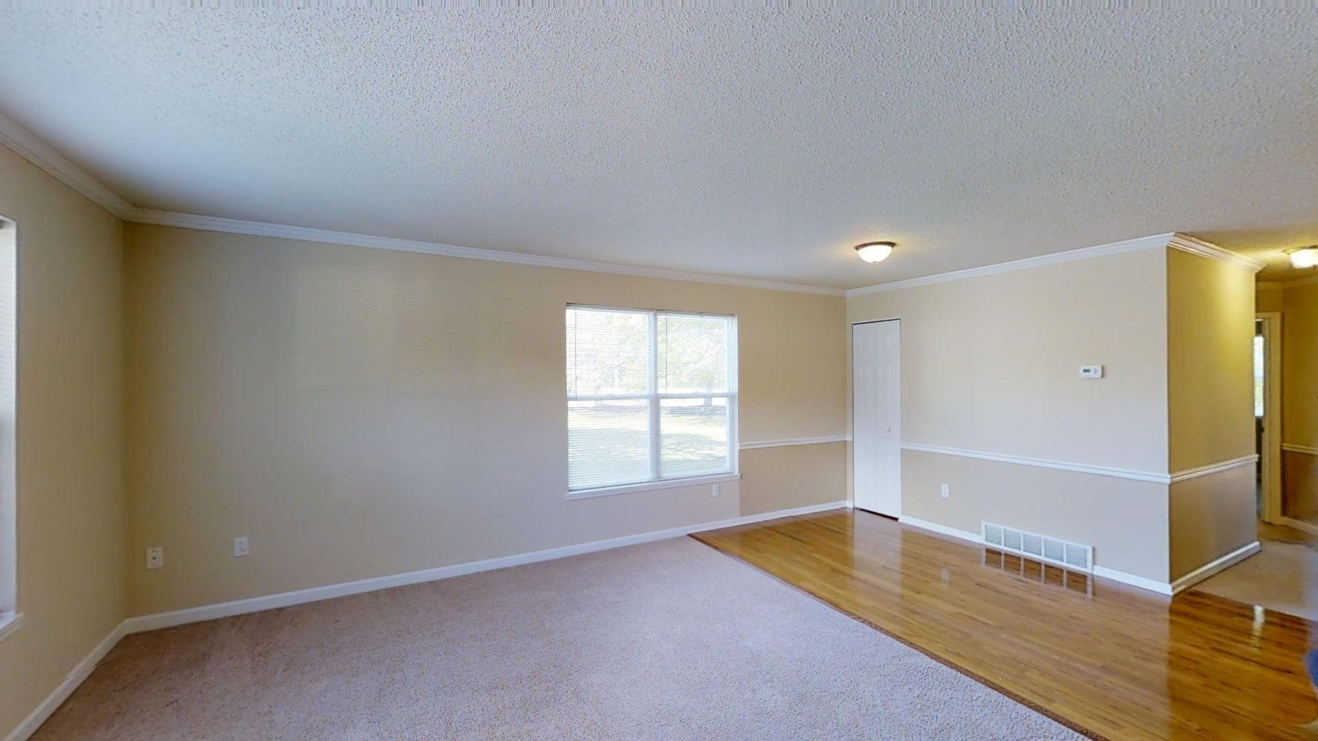 An empty living room with hardwood floors and beige walls.