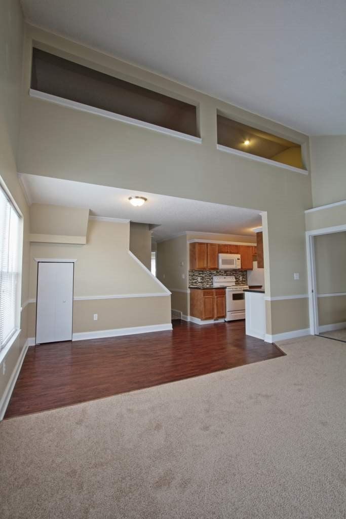 An empty living room with hardwood floors and a kitchen in the background.