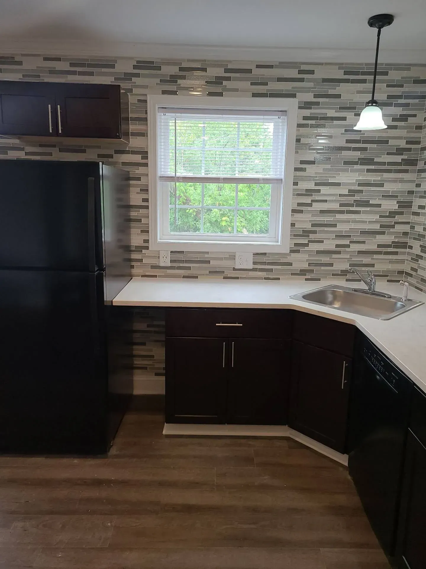A kitchen with a black refrigerator , sink , cabinets and a window.