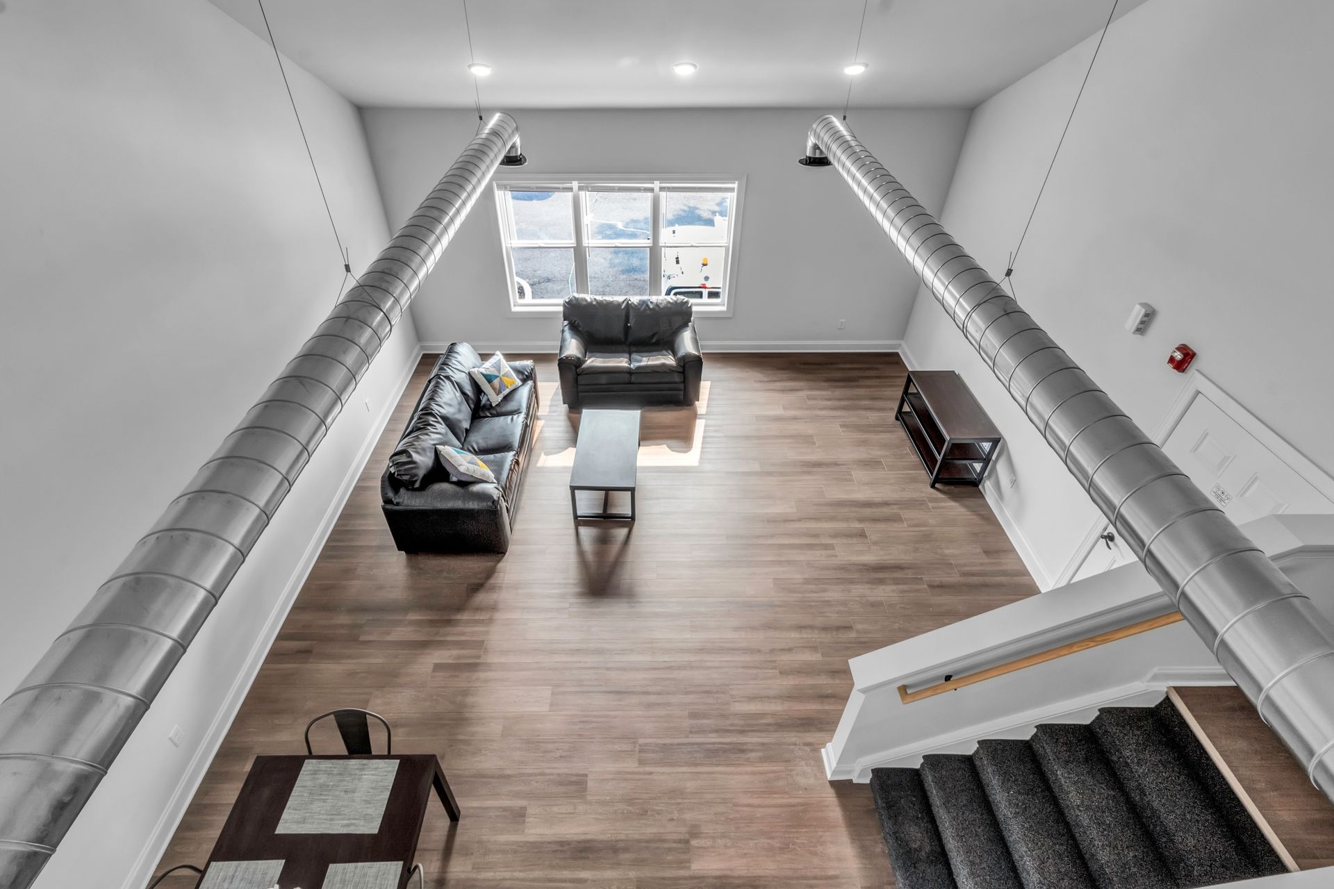 An aerial view of a living room with a couch , chair , table and stairs.
