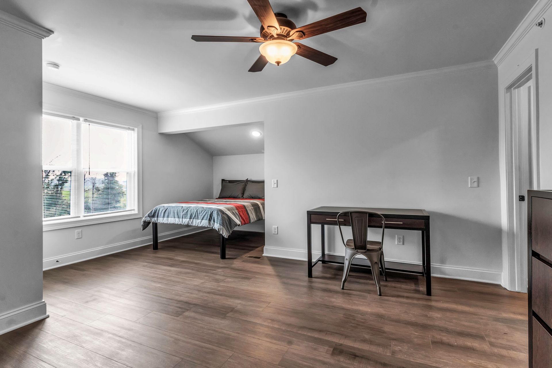 A bedroom with a bed , desk and ceiling fan.