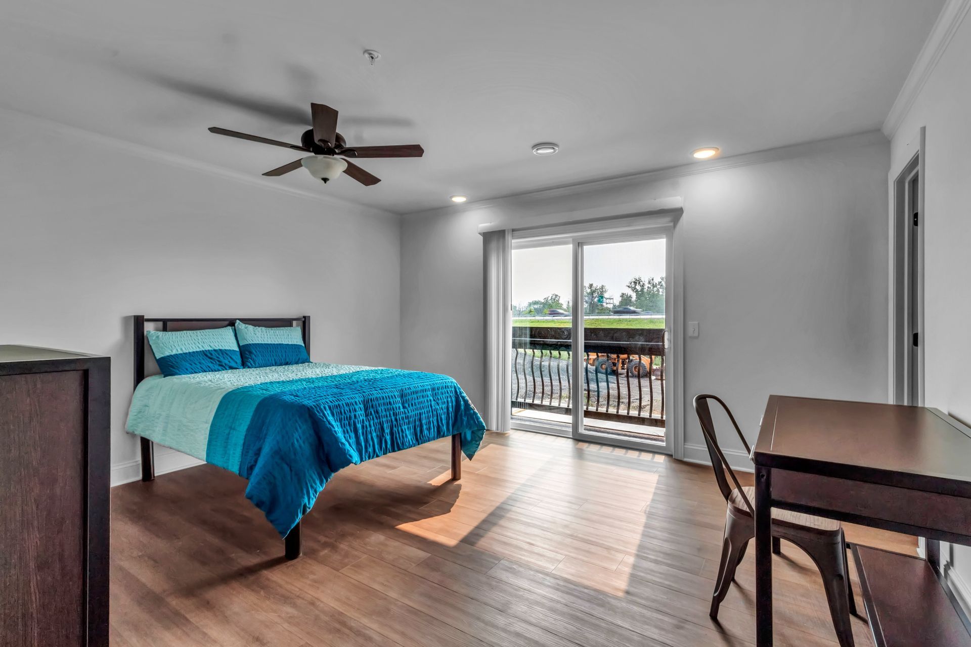 A bedroom with a bed , desk , chairs and a ceiling fan.