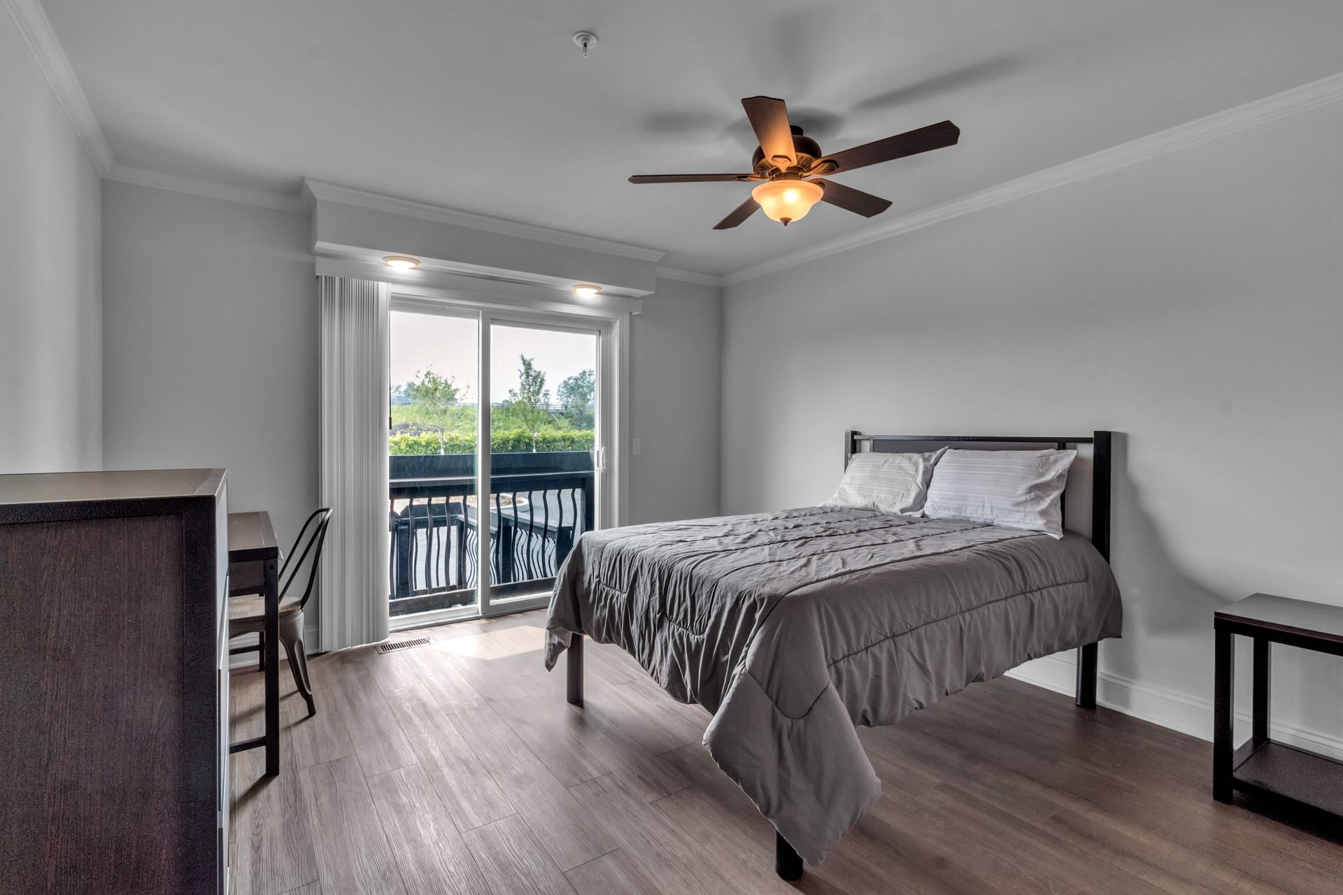 A bedroom with a bed , desk , nightstand and ceiling fan.
