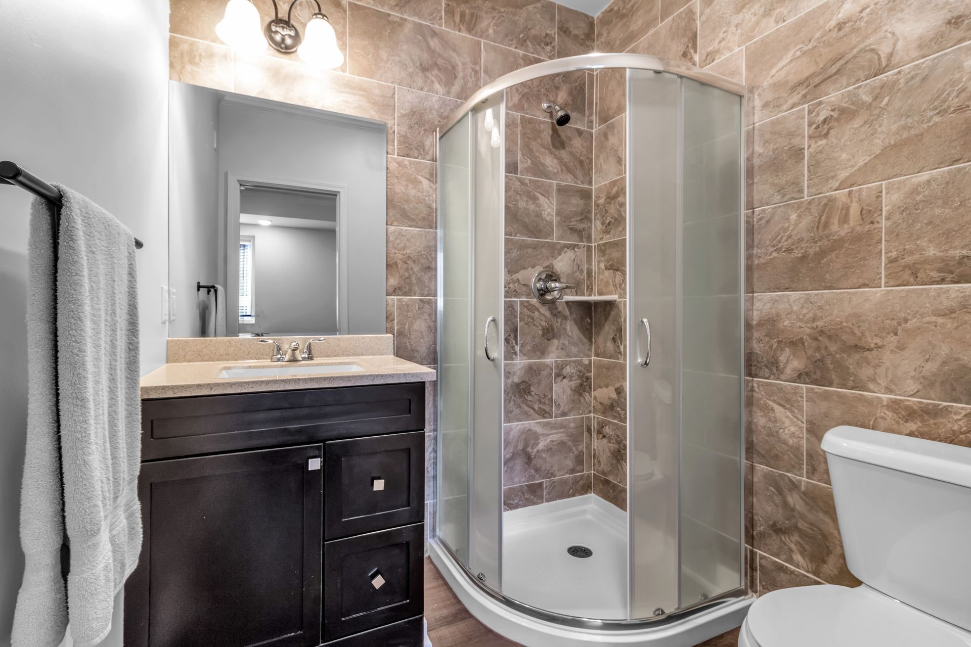 A bathroom with a shower , sink , toilet and mirror.