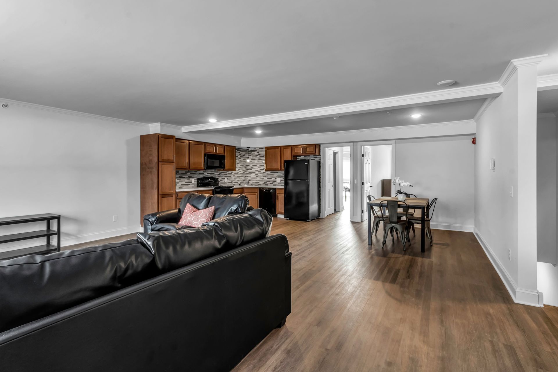A living room with a black couch , wooden floors , and a kitchen.