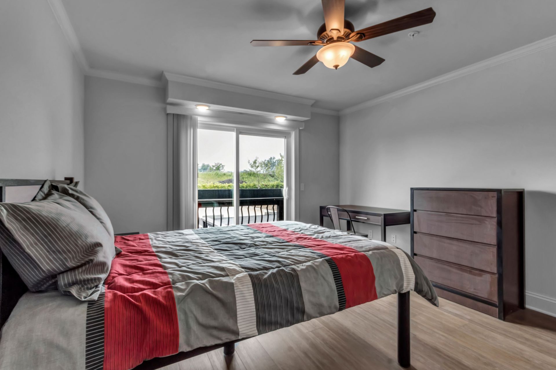 A bedroom with a bed , dresser , desk and ceiling fan.