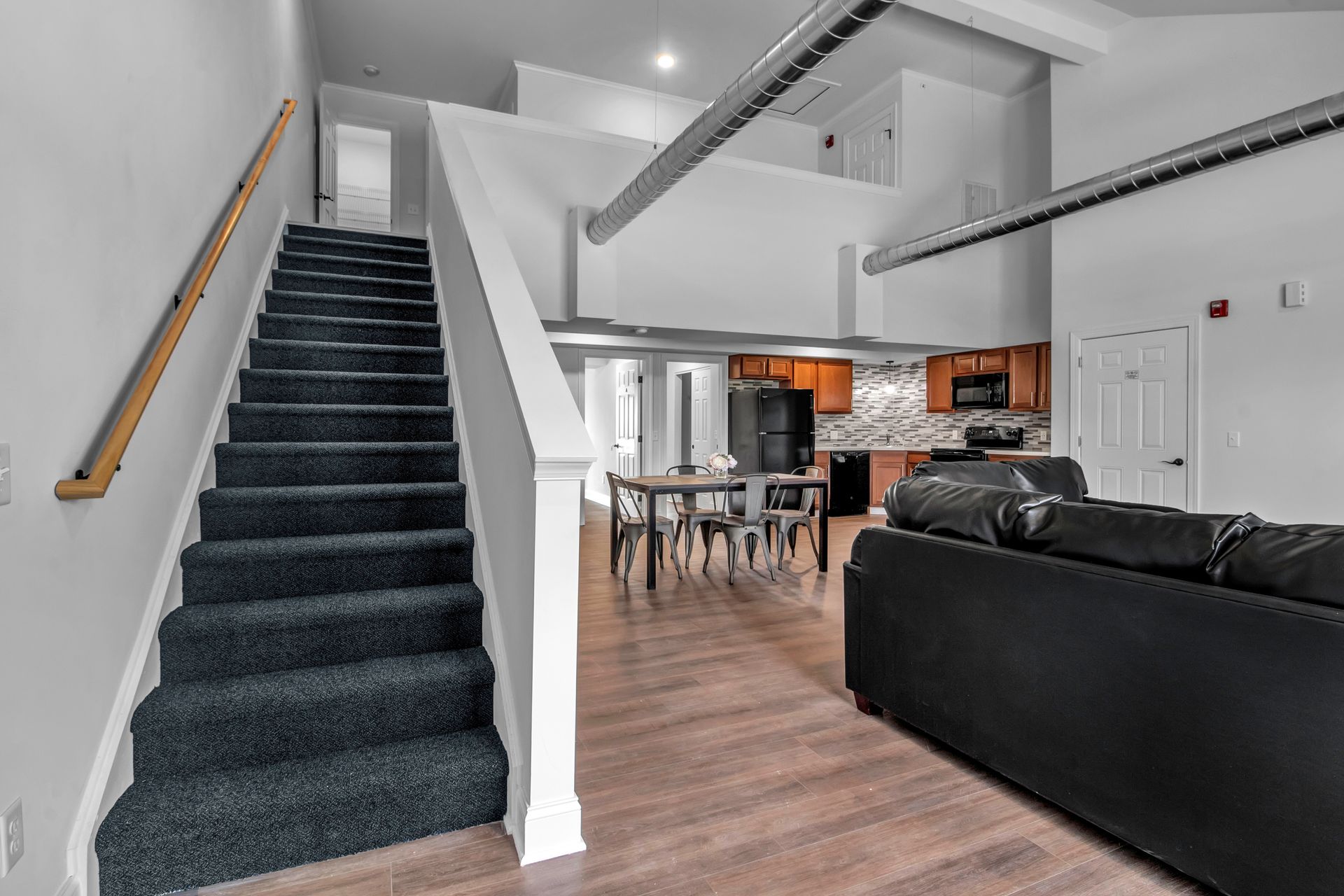 A living room with stairs leading up to the second floor and a black couch.