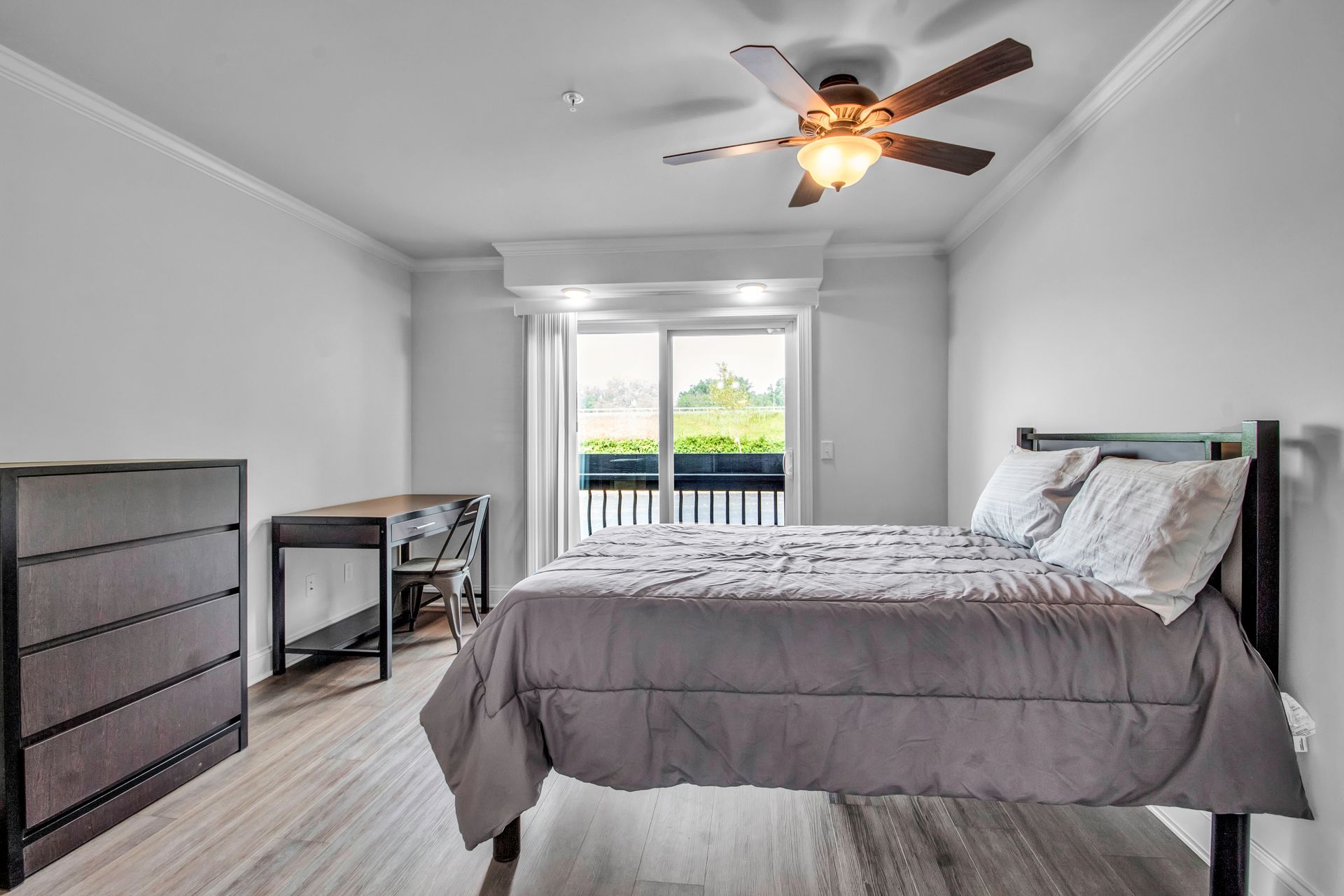 A bedroom with a bed , dresser , desk and ceiling fan.