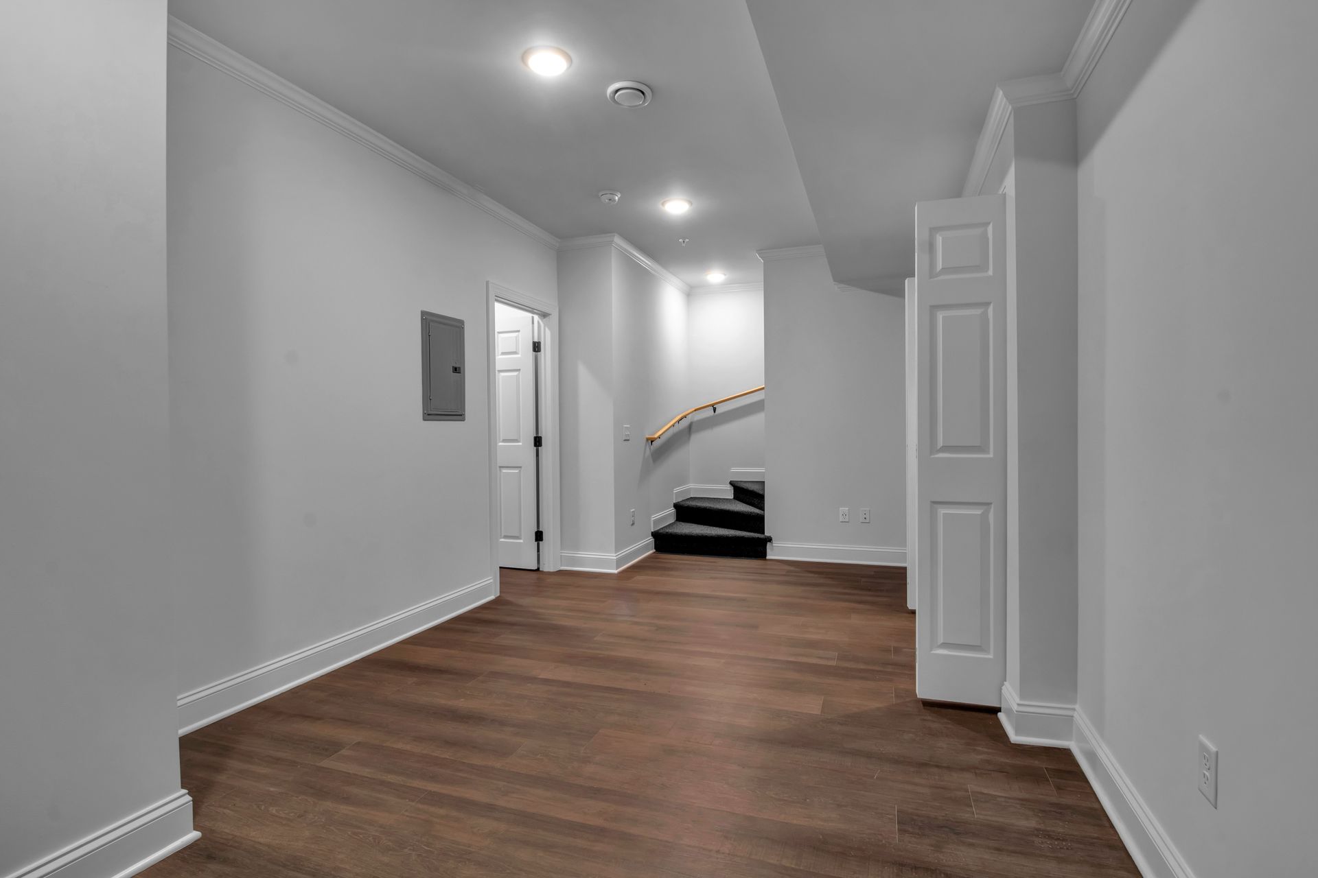 An empty basement with hardwood floors and white walls.