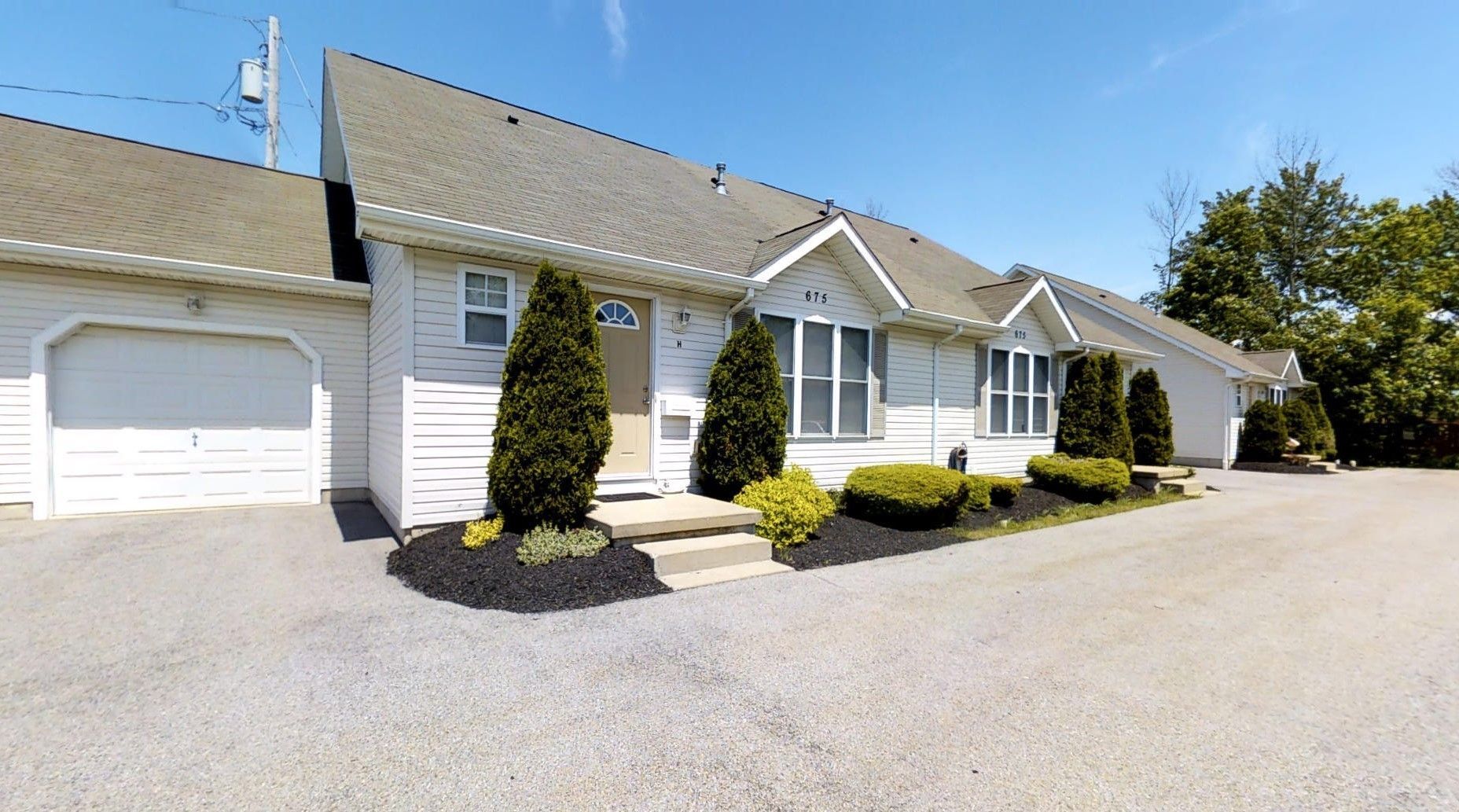 A row of white houses with garages and trees in front of them.