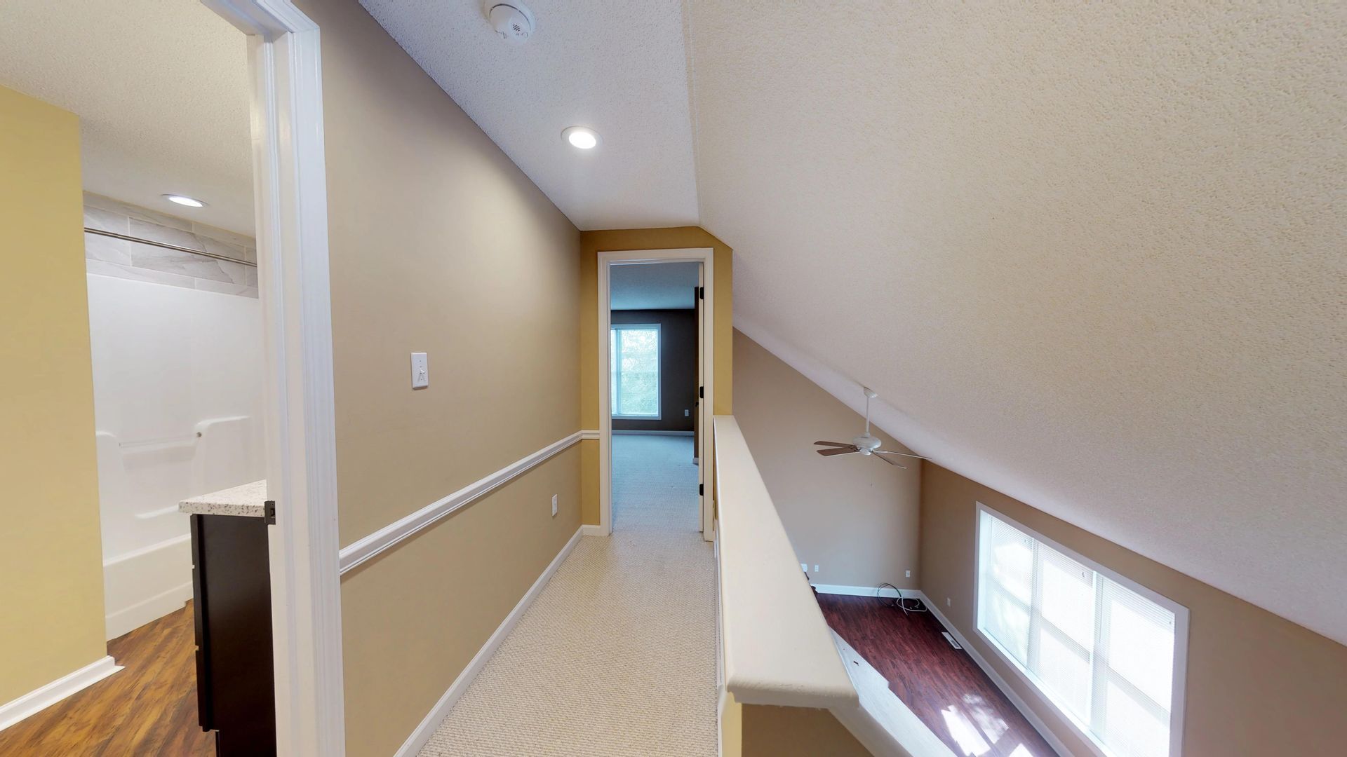 A hallway in a house with a ceiling fan and a window.