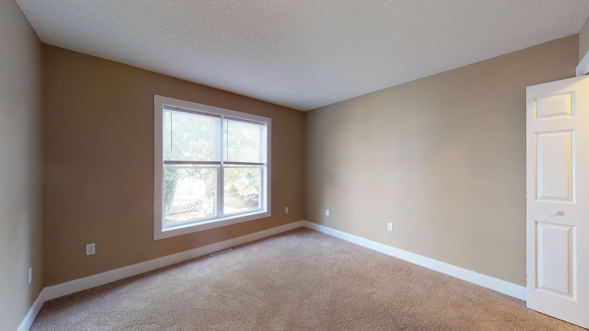 An empty bedroom with a window and a carpeted floor.