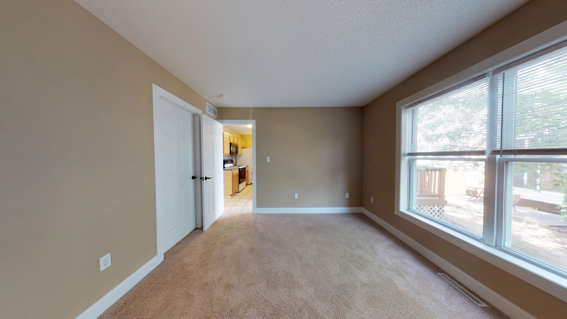 An empty living room with a lot of windows and a carpeted floor.