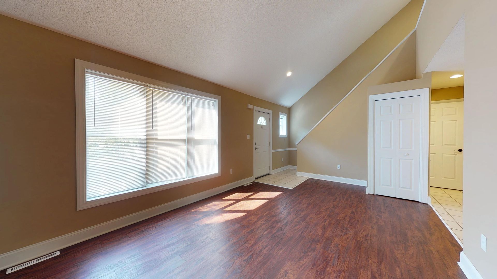 An empty living room with hardwood floors and a vaulted ceiling.