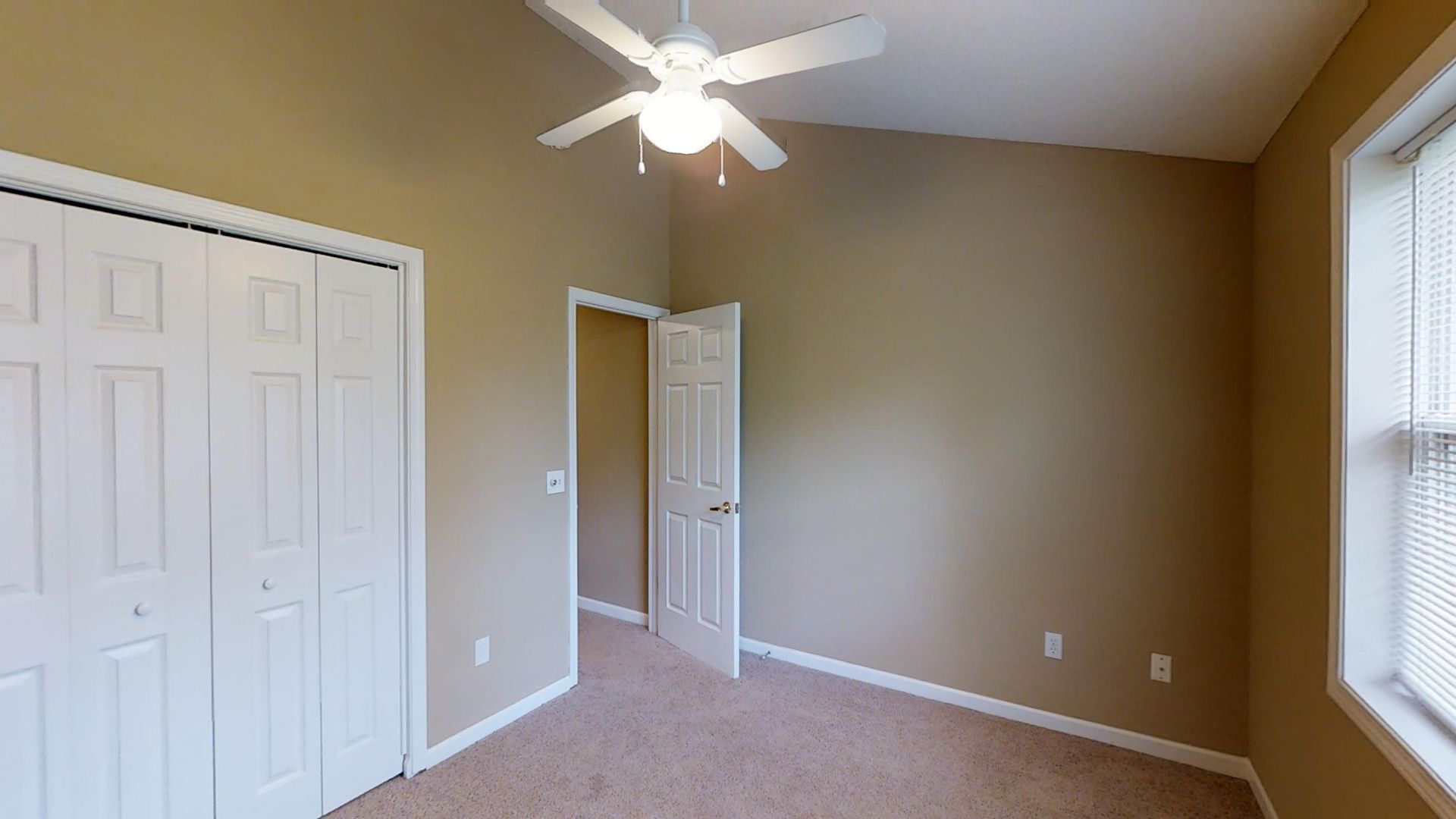 An empty bedroom with a ceiling fan and a window.