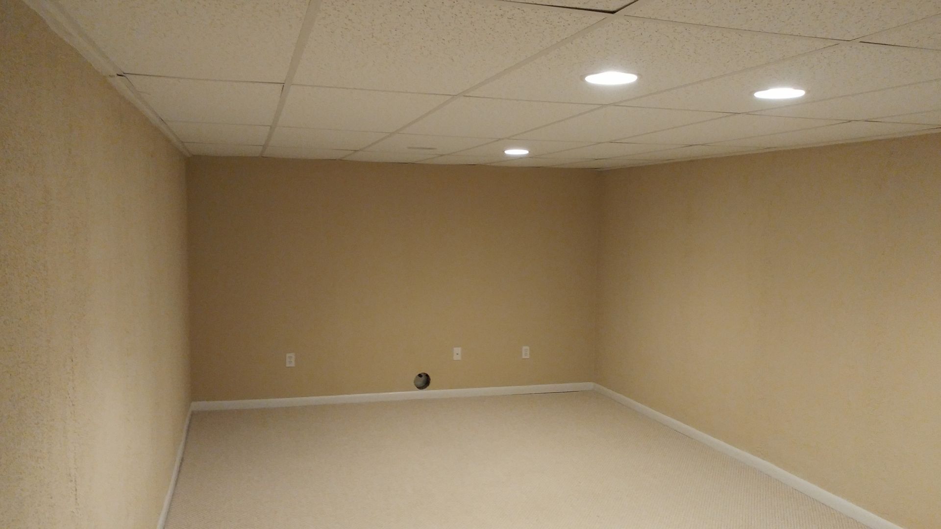 An empty basement with tan walls and white carpet.