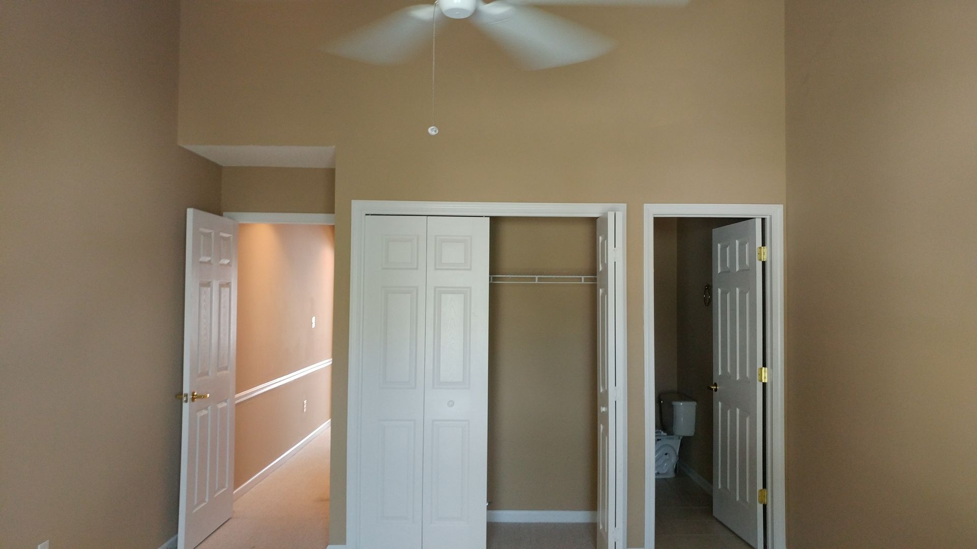 An empty bedroom with a ceiling fan hanging from the ceiling.