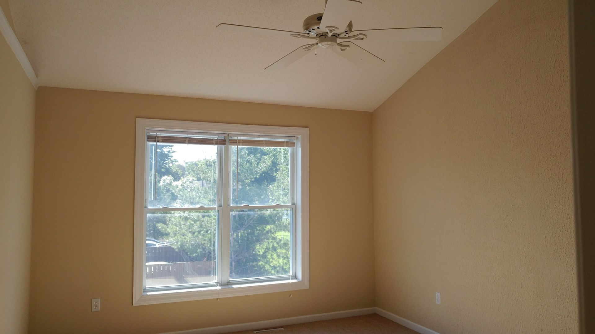 An empty room with a window and a ceiling fan.